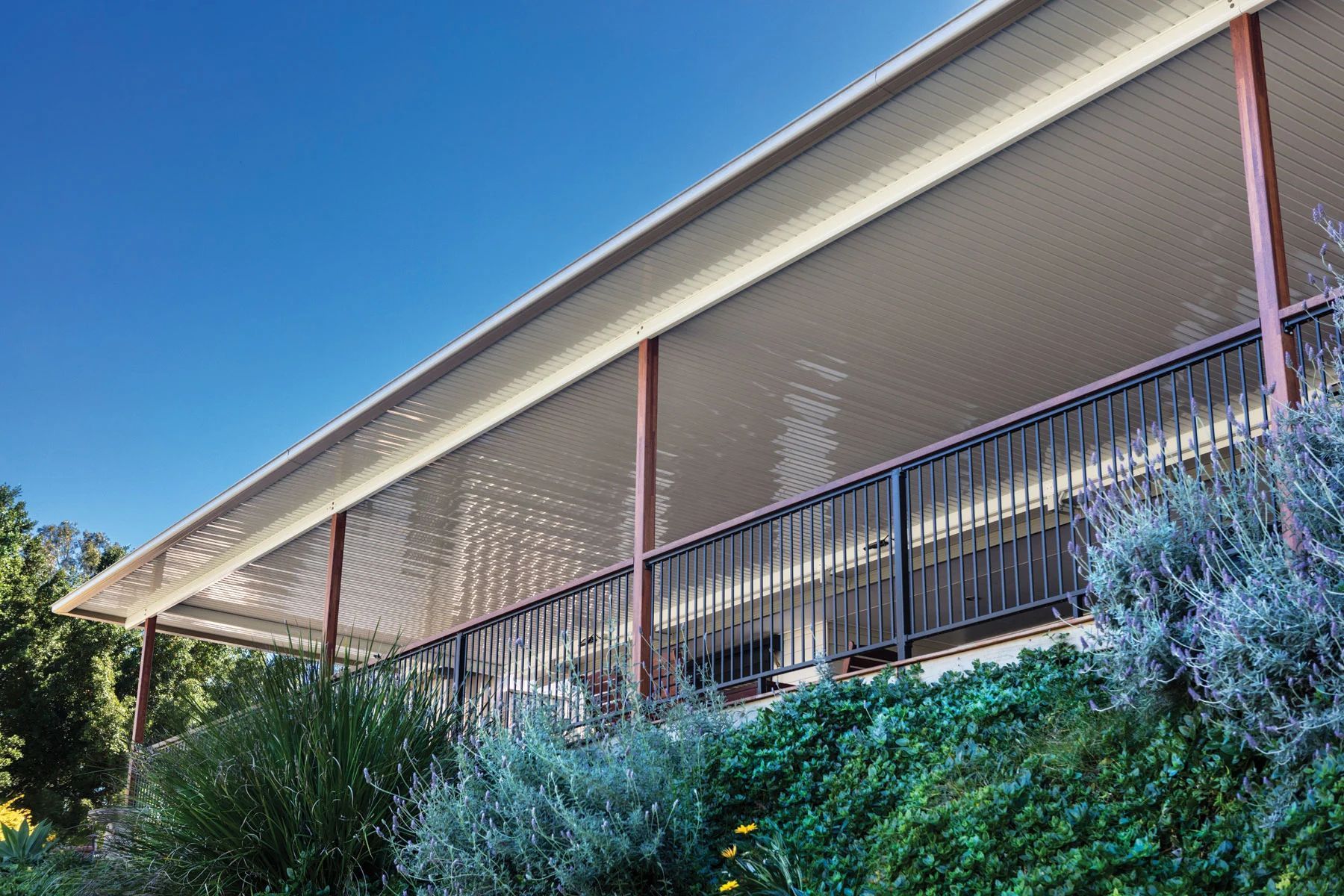 Modern building with a slanted roof, red columns, and a shaded balcony above dense greenery