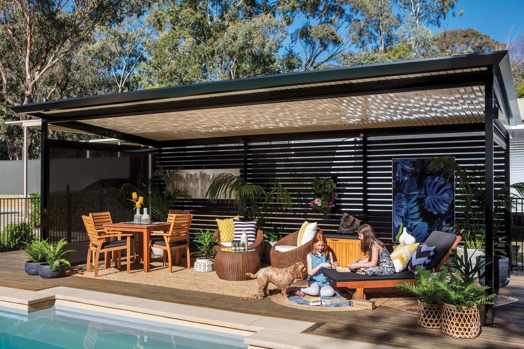 Patio lounge by a pool with wooden furniture, umbrellas, plants, and people relaxing under a pergola