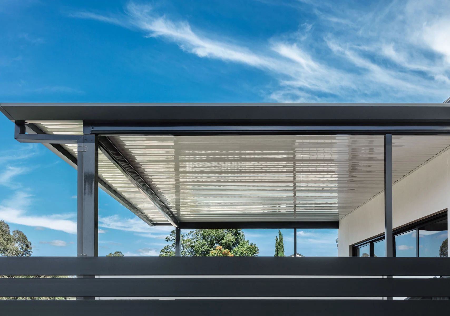 Modern house patio with a flat roof, metal beams, and a blue sky overhead