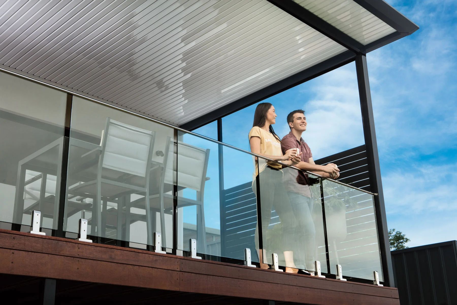 Two people standing on a modern balcony, holding drinks and looking out at the view.