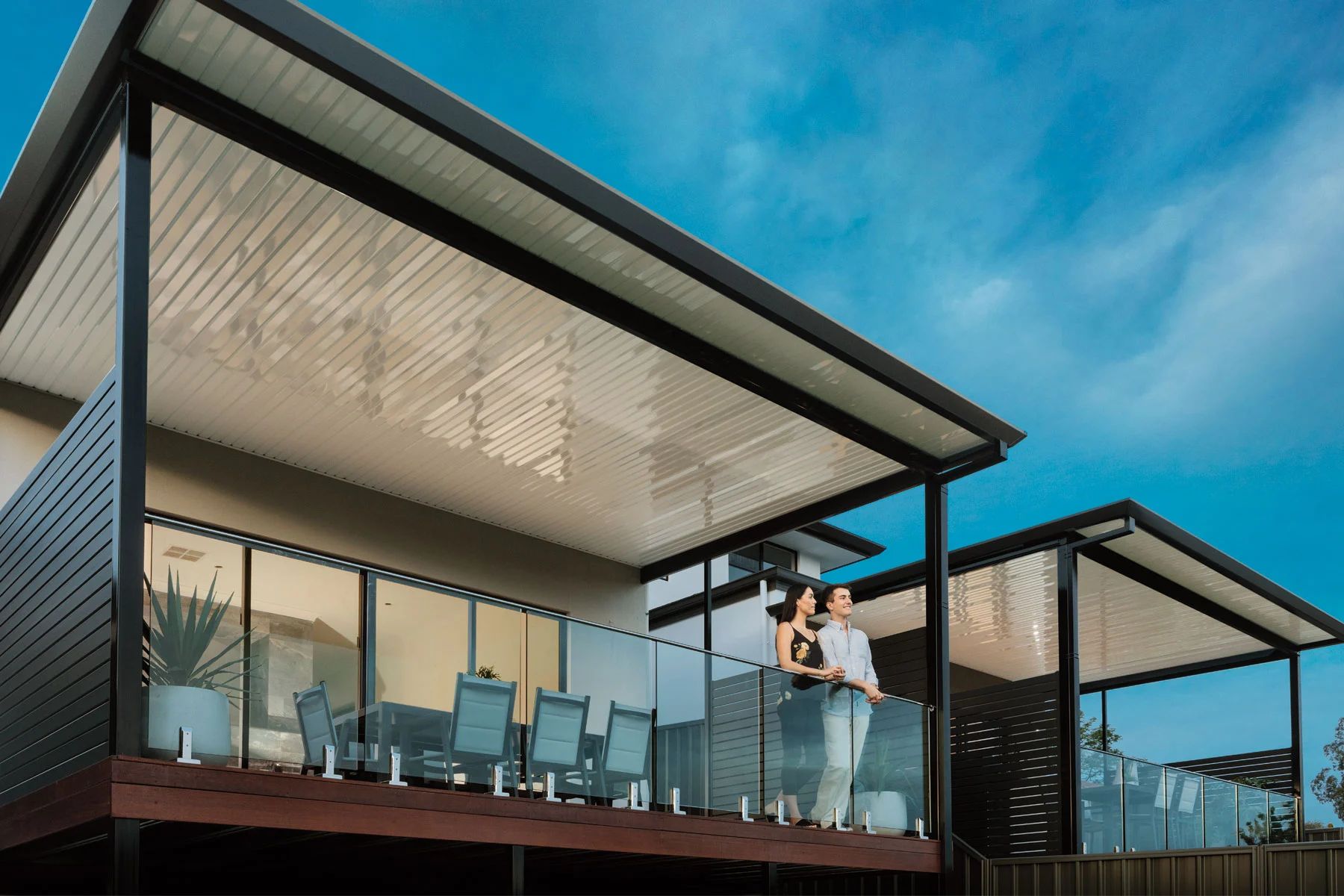 Modern house with glass balcony and patio chairs under a blue sky
