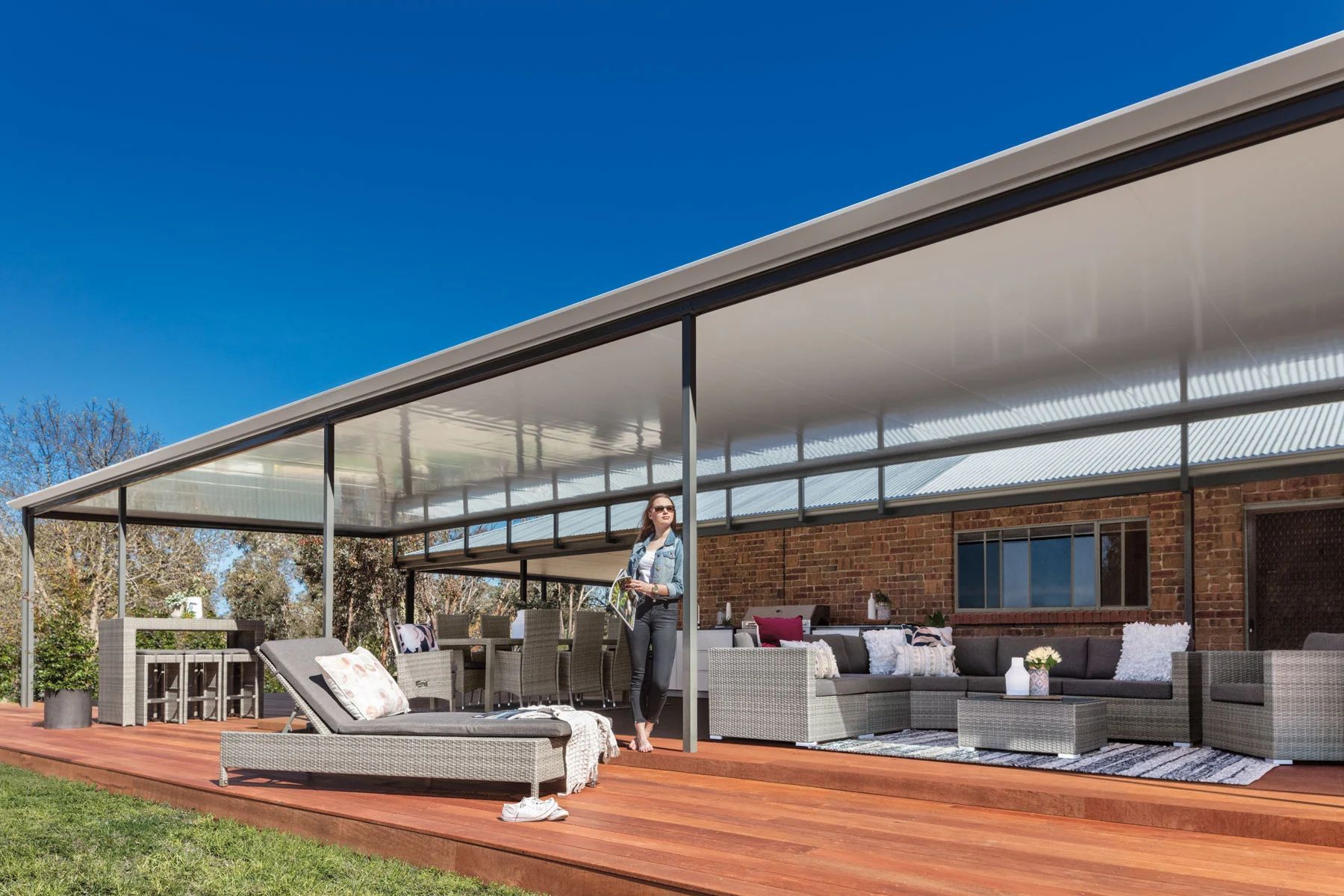Covered outdoor patio with modern seating and lounge chairs on a wooden deck under a clear blue sky