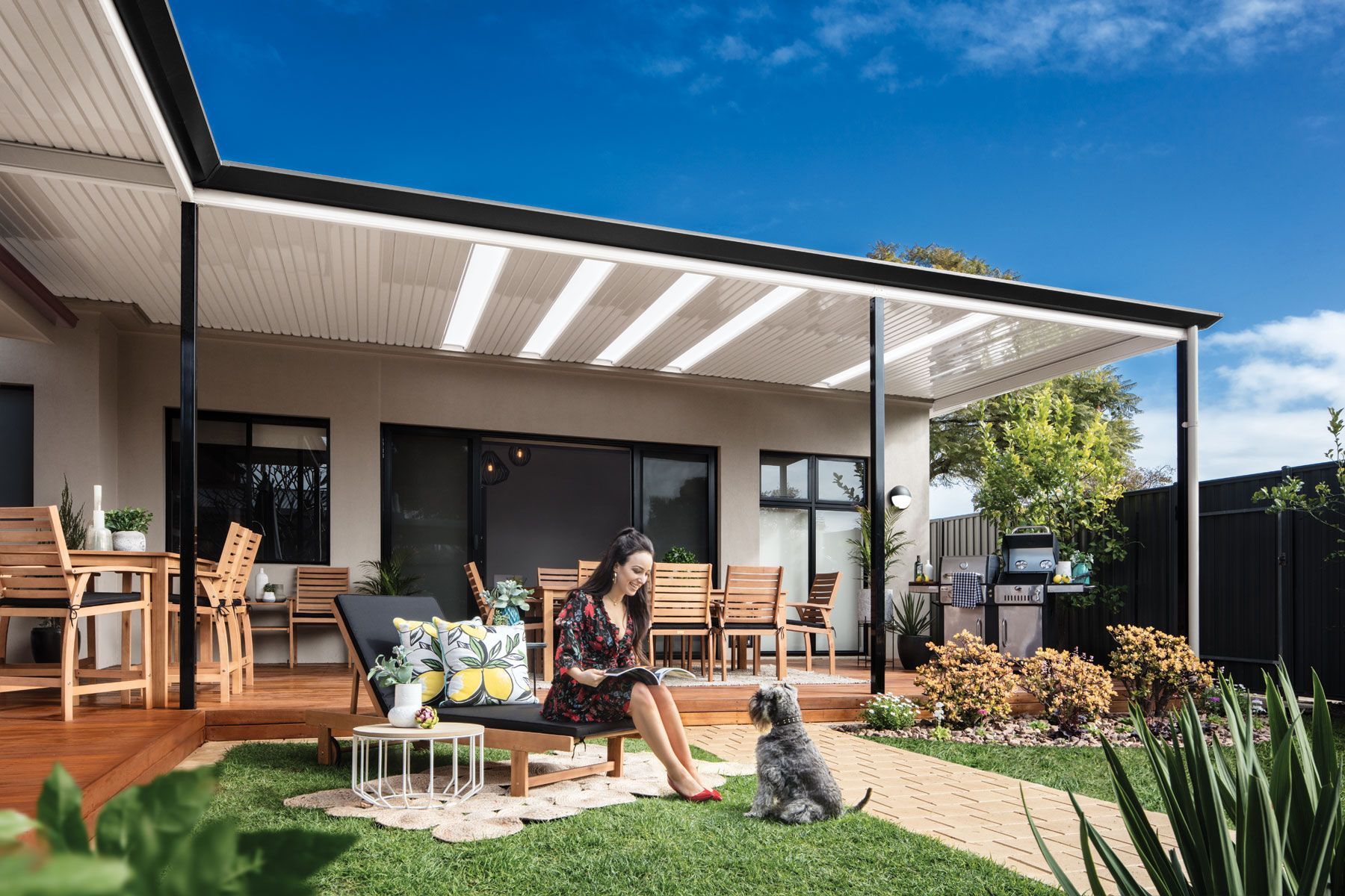 Backyard patio with two people relaxing on a modern deck beside a green lawn and house