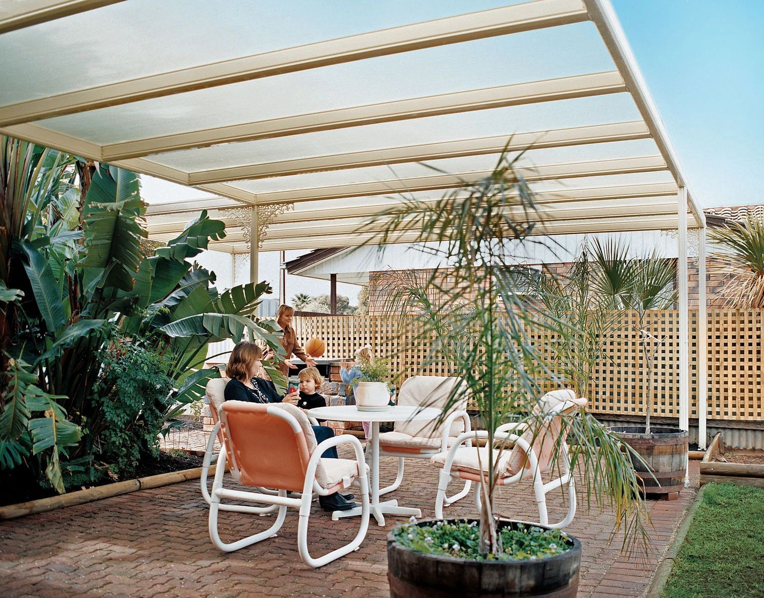 Outdoor patio with white pergola, orange chairs, and potted plants beside a garden wall