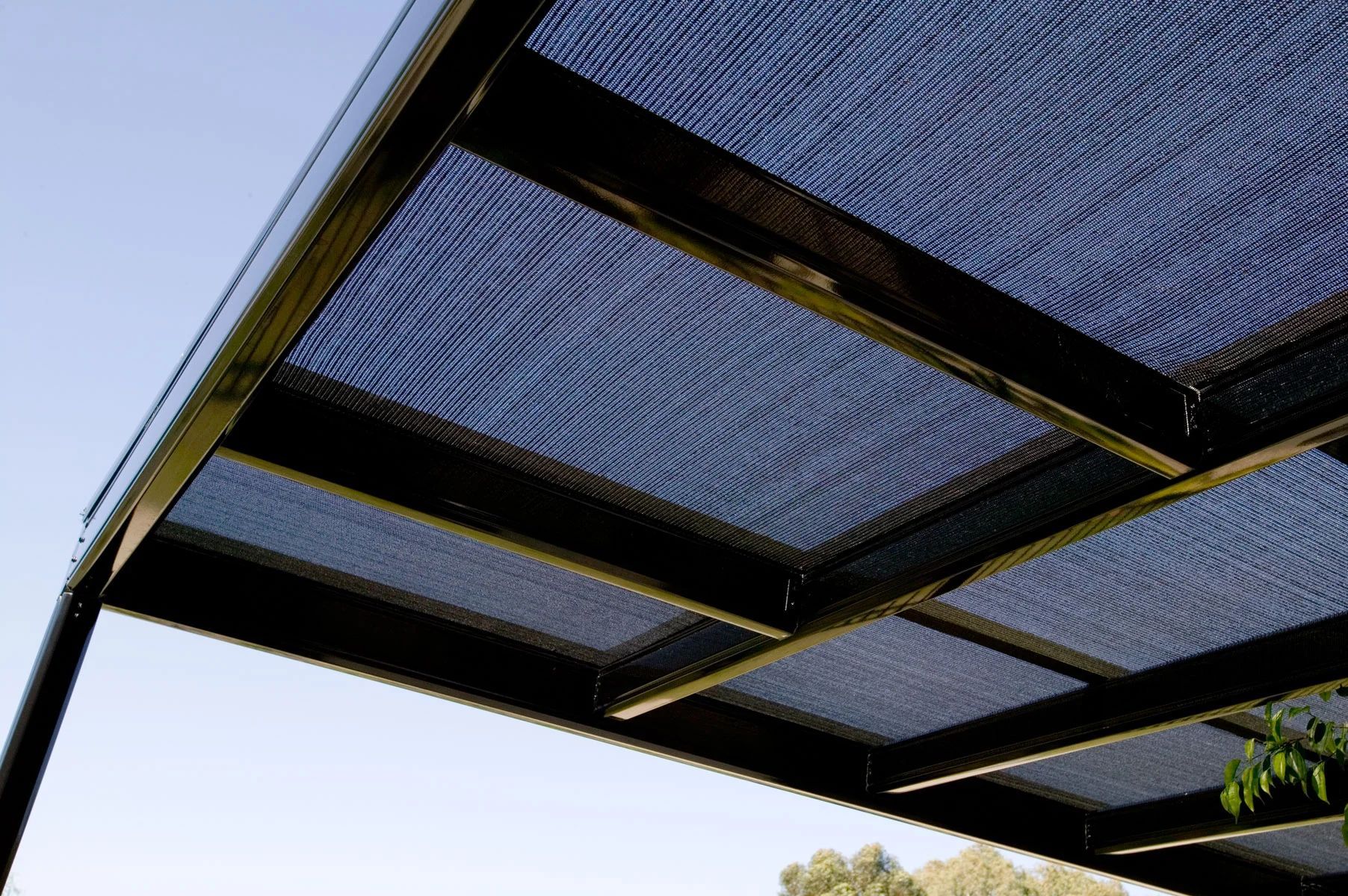 Black metal pergola roof with blue mesh panels against a clear sky