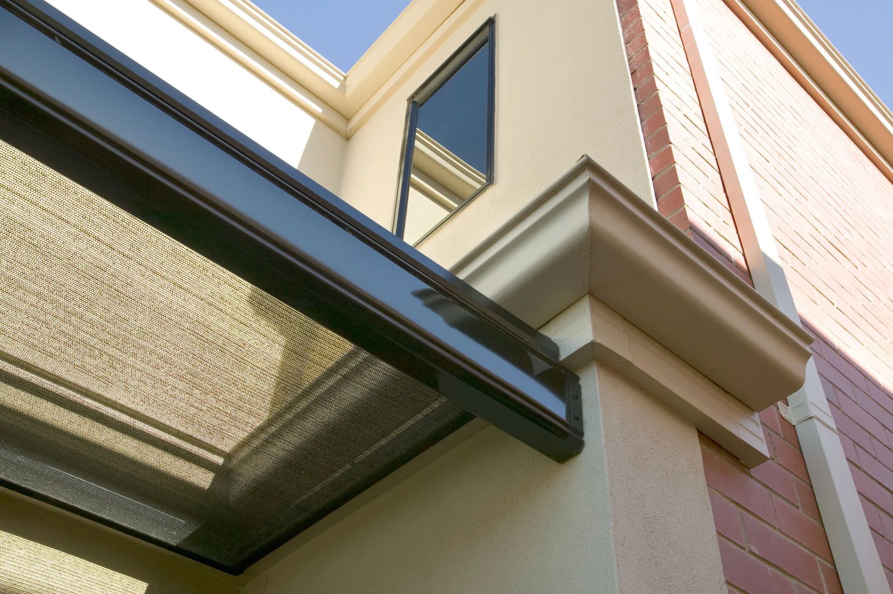 Modern building exterior with beige stucco, brick accents, and a dark metal awning under blue sky