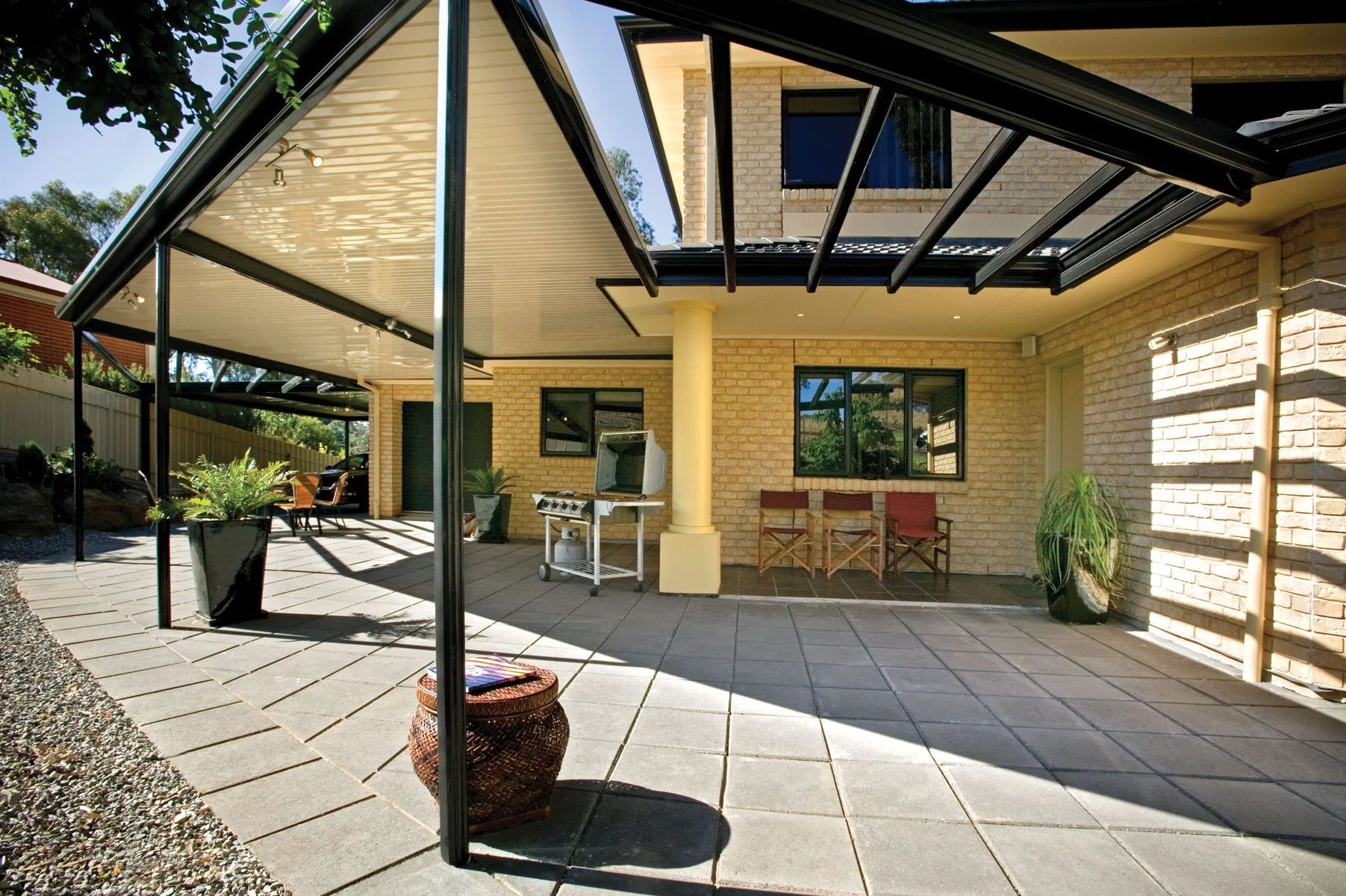 Covered outdoor patio with black pergola, brick wall, tables, chairs, and potted plants