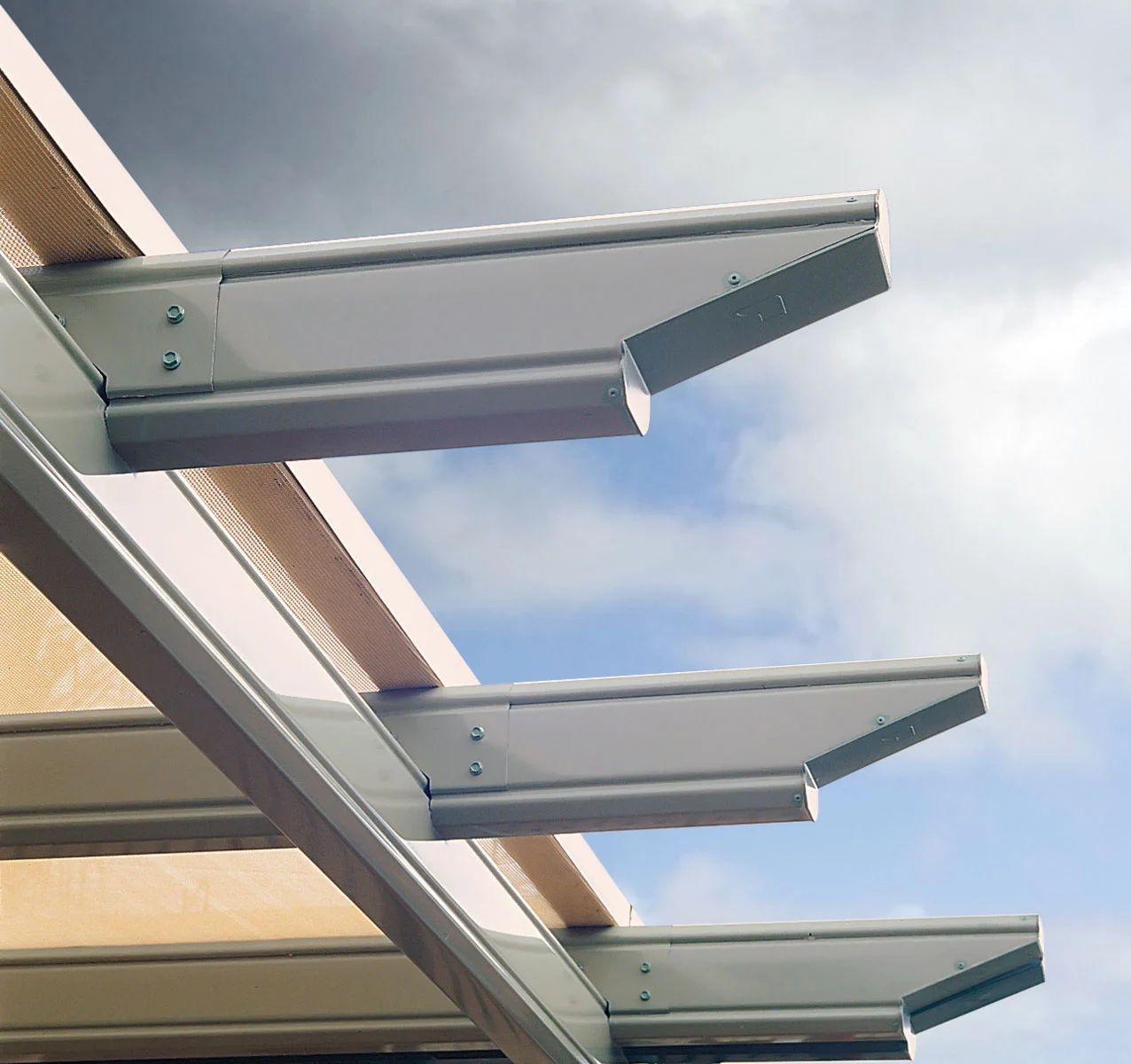 Three metal awning brackets extending from a building against a cloudy sky