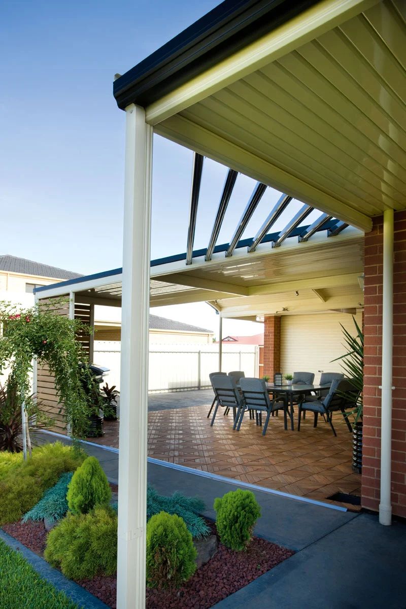Patio with brick floor, outdoor table and chairs, and white awning beside a house garden