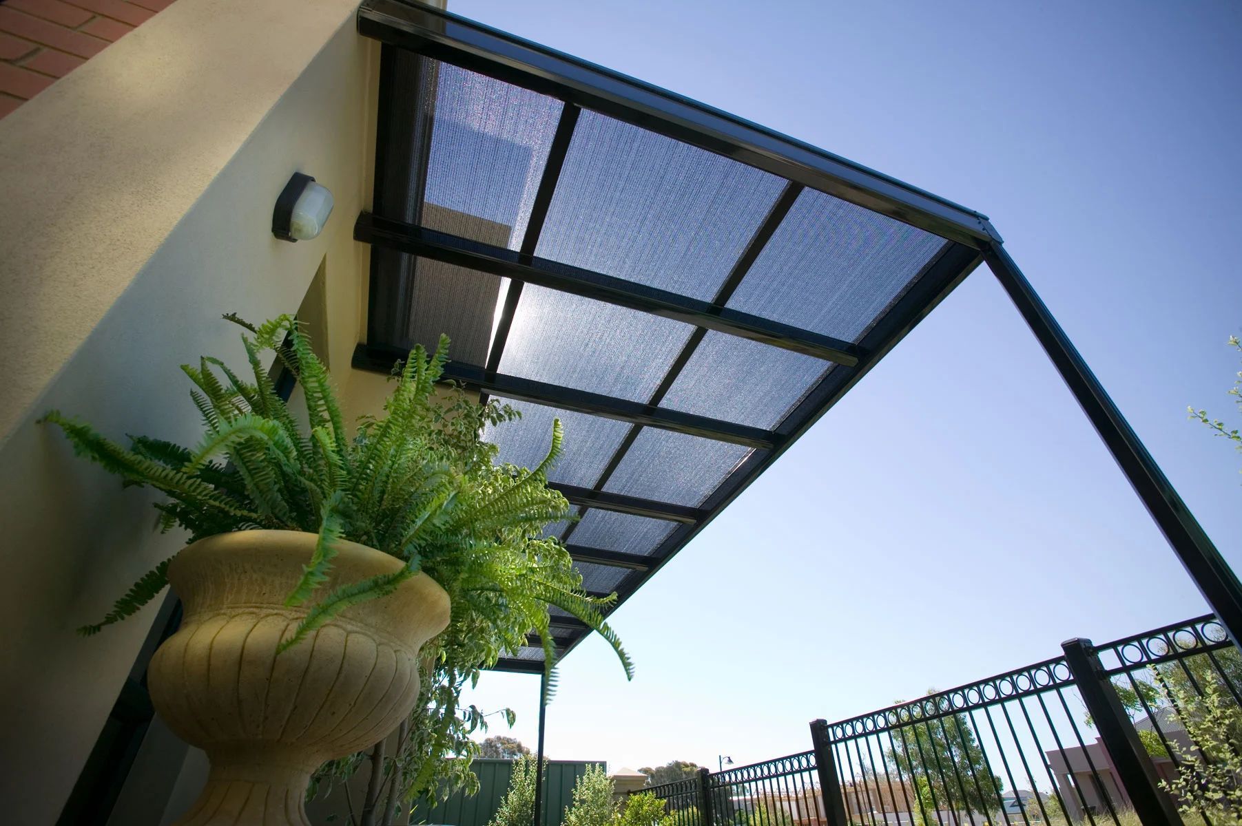 Covered patio with black metal awning, hanging planter, and blue sky overhead