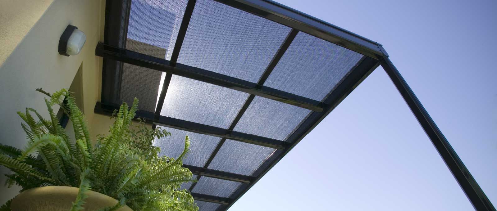 Black metal canopy with translucent roof panels beside green palm fronds against a blue sky