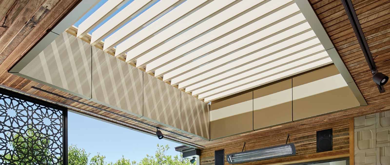 Open retractable patio pergola with white slats over a brick patio and blue sky beyond
