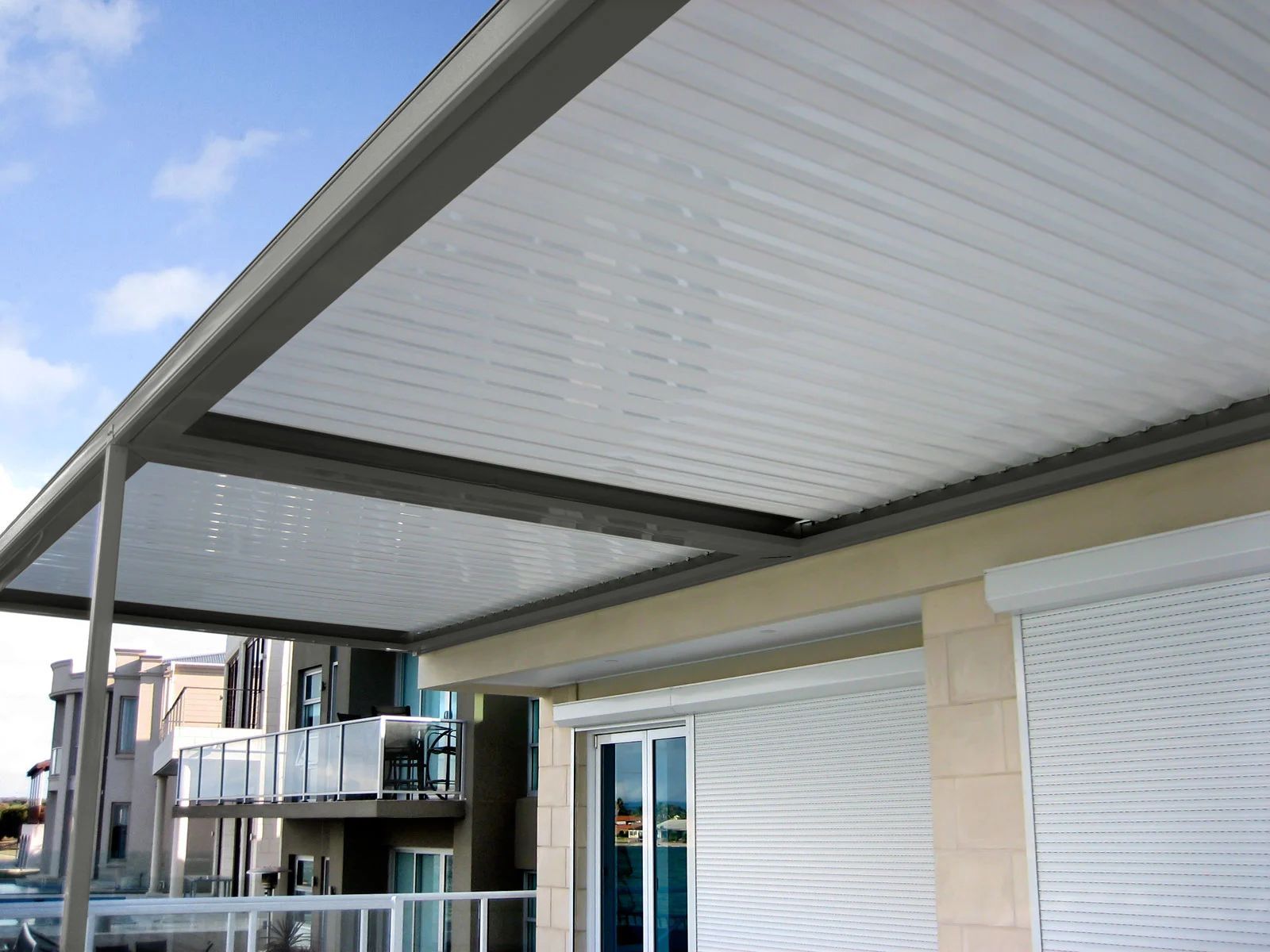 Covered patio with a white ceiling and gray beams beside a modern building.