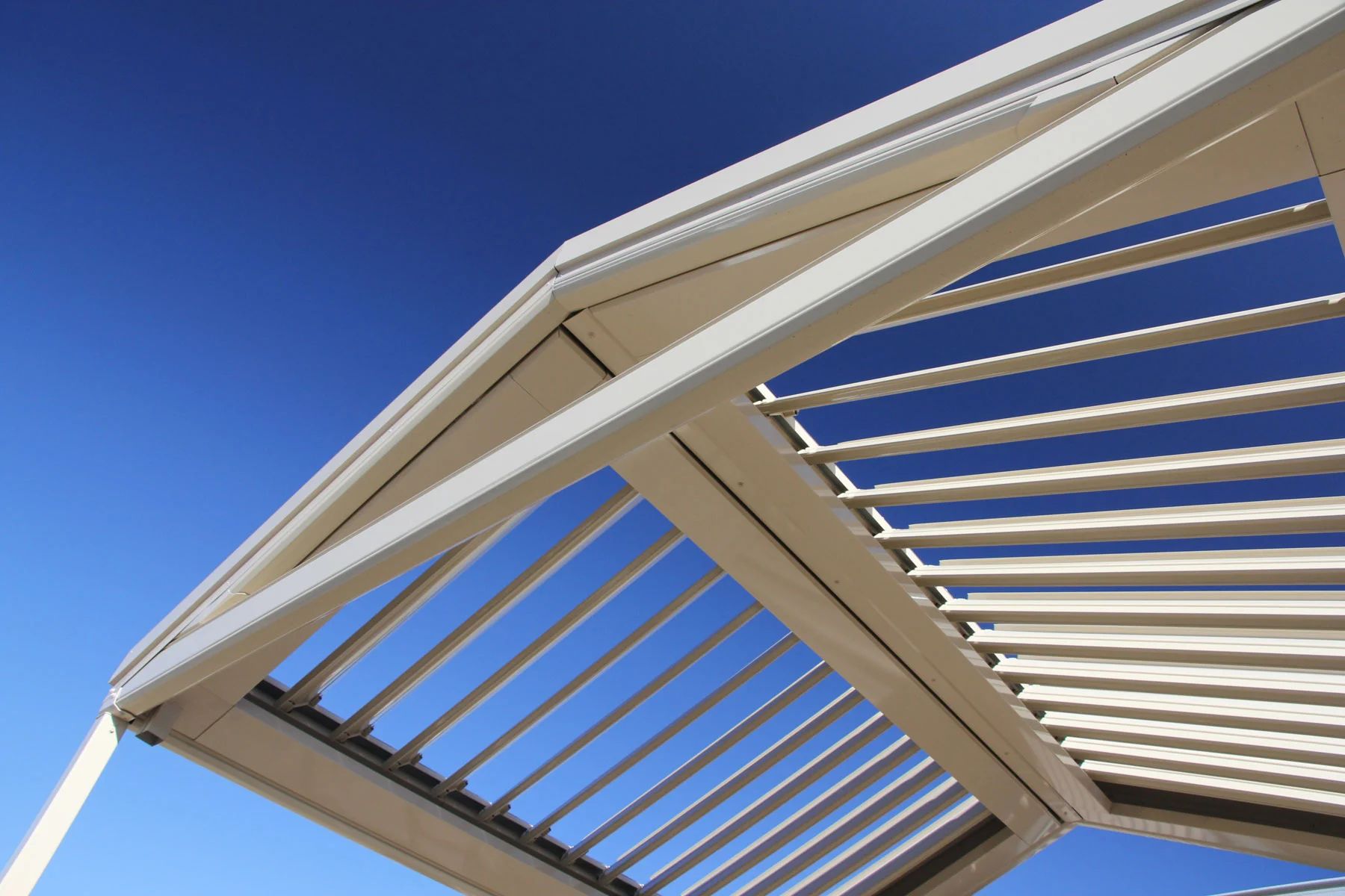 White pergola roof slats against a clear blue sky