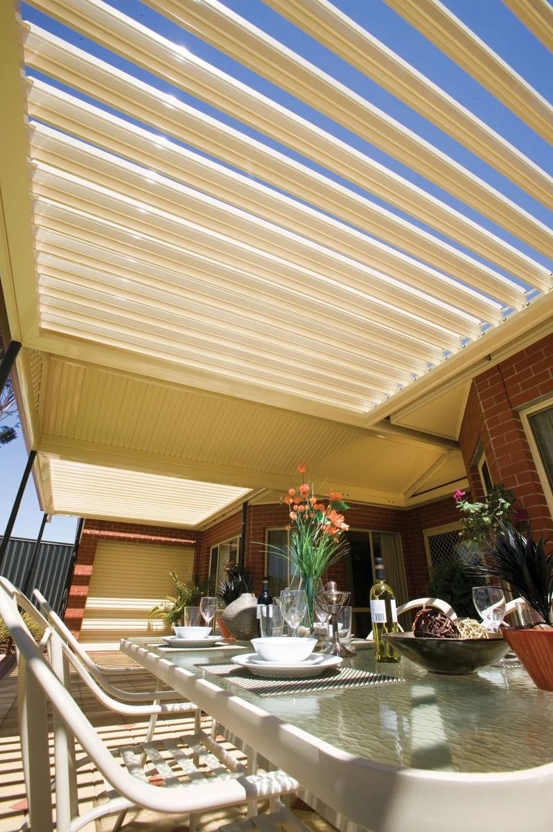 Patio dining area with striped awning, glass table, and chairs in warm sunlight
