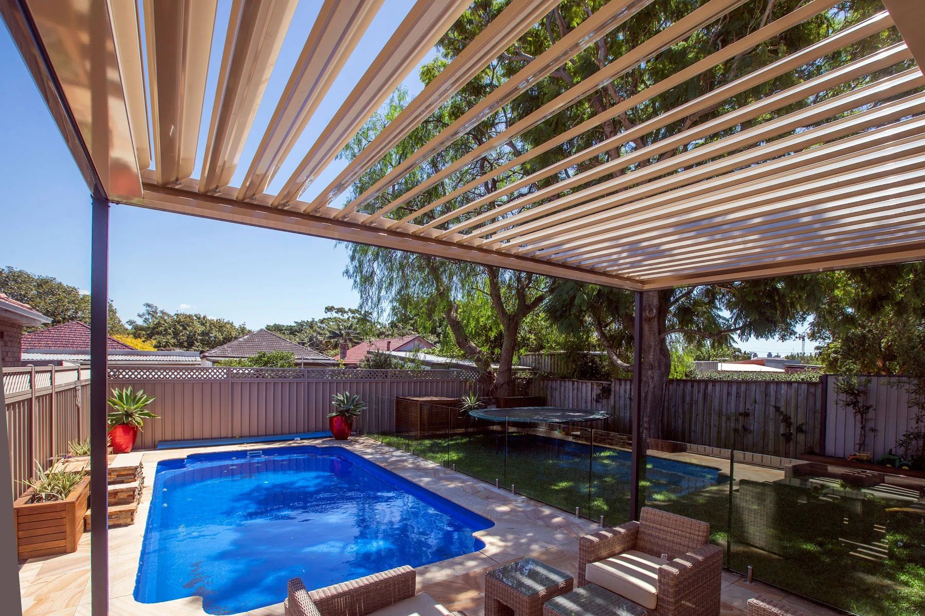 Backyard patio with a small blue pool, striped pergola, and outdoor seating under trees