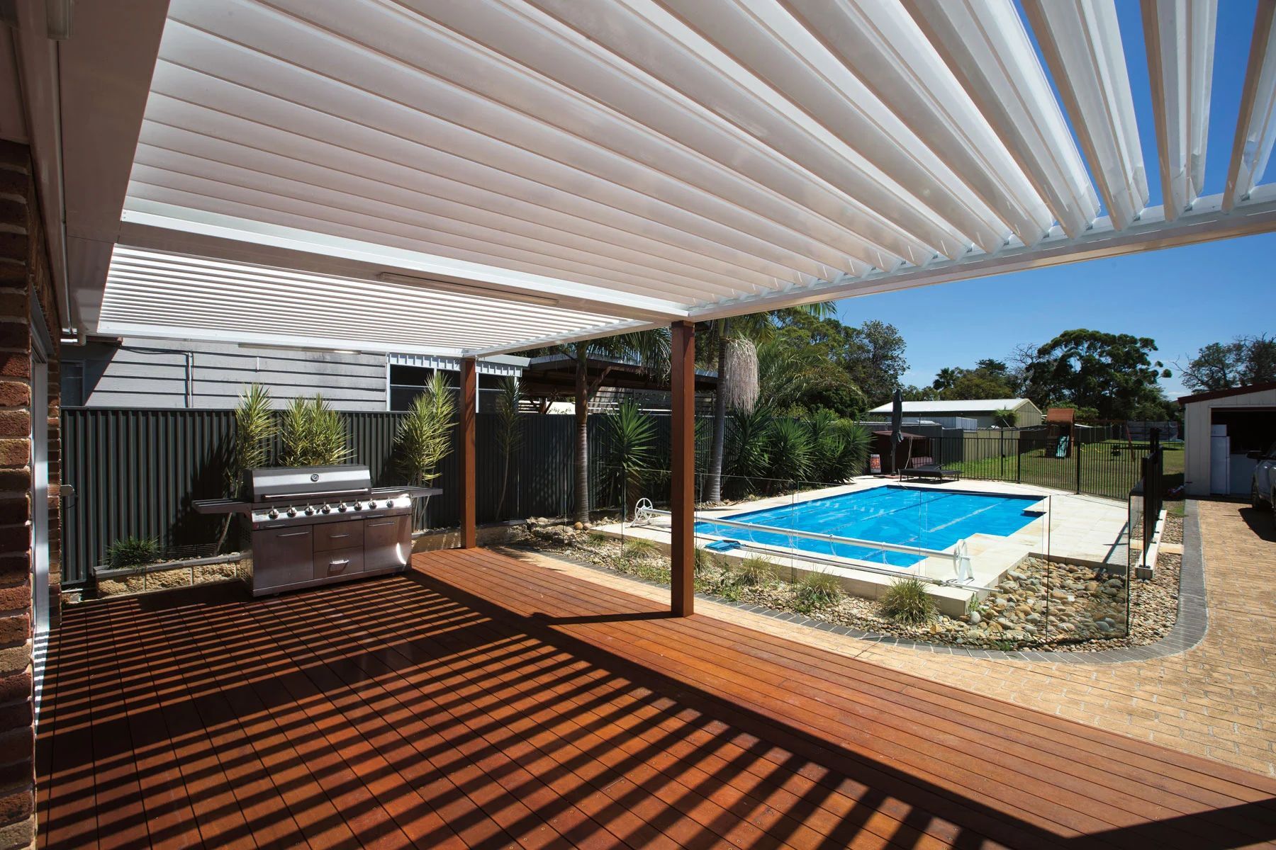 Covered patio with pergola, pool, and backyard view in bright sunlight