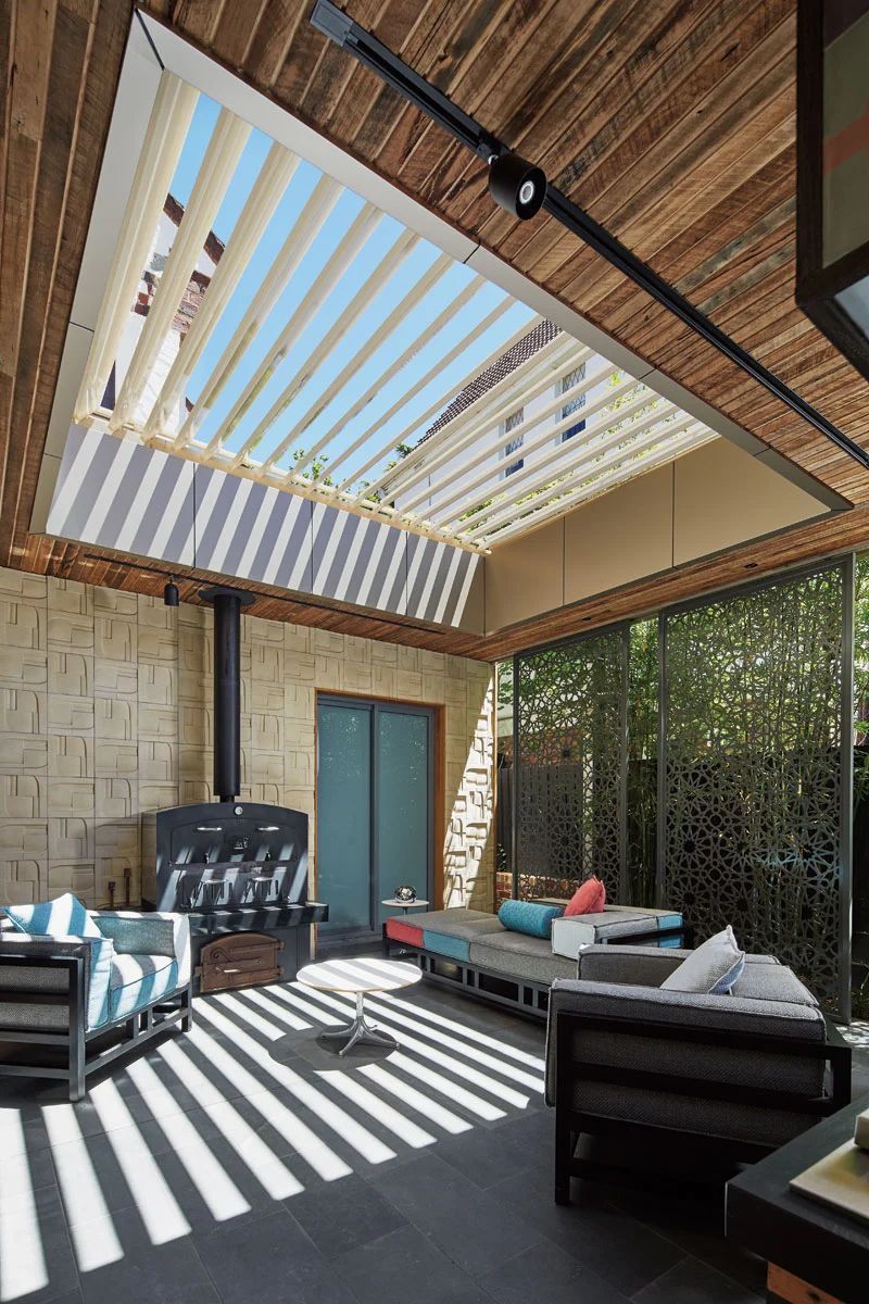 Covered patio with striped sunlight, outdoor sofas, a table, and a green door under a slatted roof