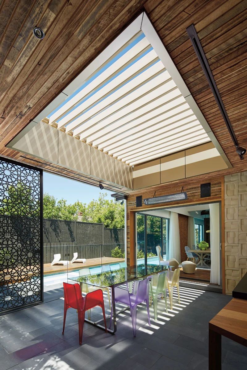 Modern patio with a retractable awning, colorful chairs, and sliding glass doors opening to a pool area