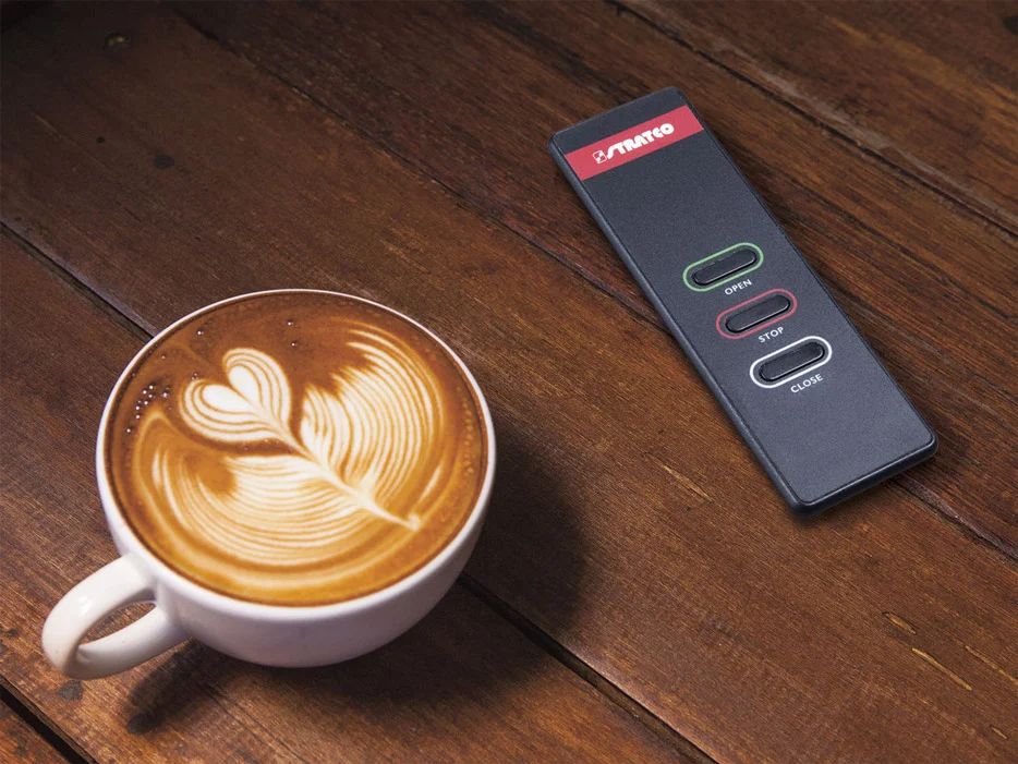 Latte with leaf art beside a black remote on a wooden table