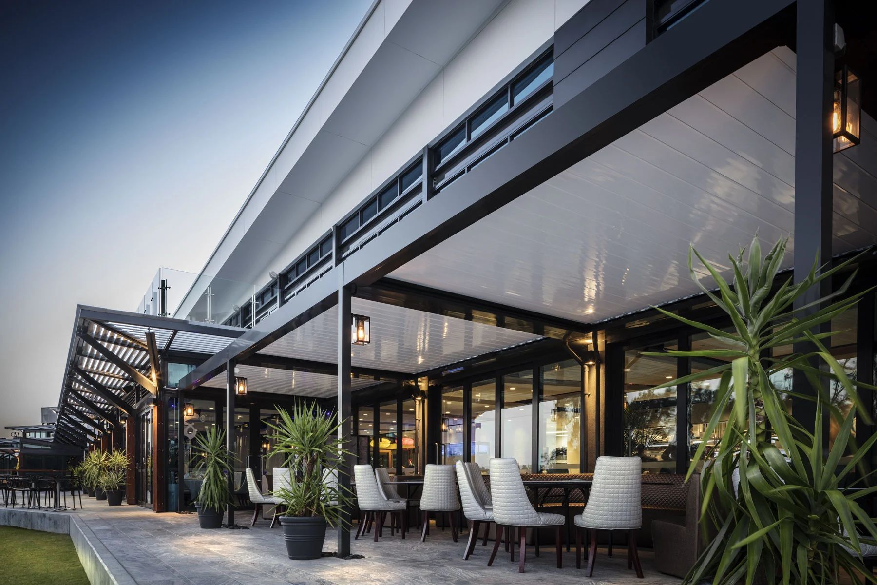 Modern outdoor restaurant patio with white chairs, black awnings, and potted palm plants
