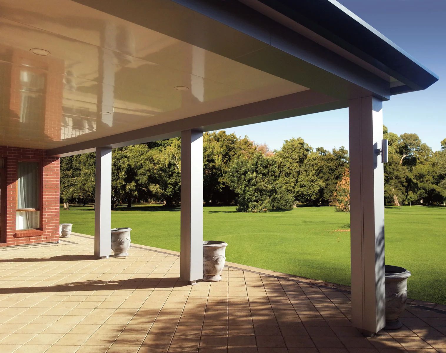 Covered patio with brick columns overlooking a sunny green lawn and trees.