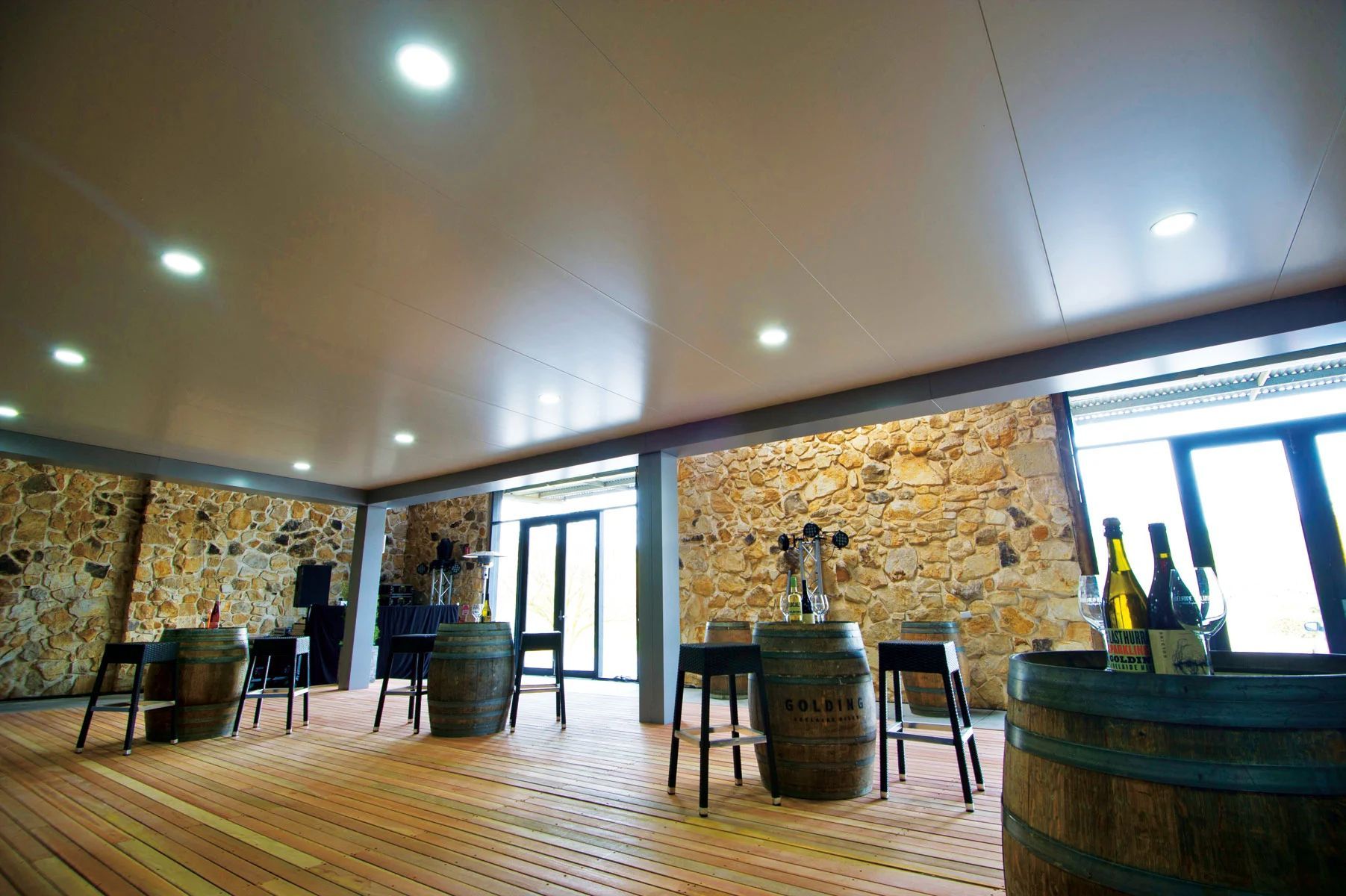 Bright lounge with stone walls, wooden floor, barrel tables, and large windows.