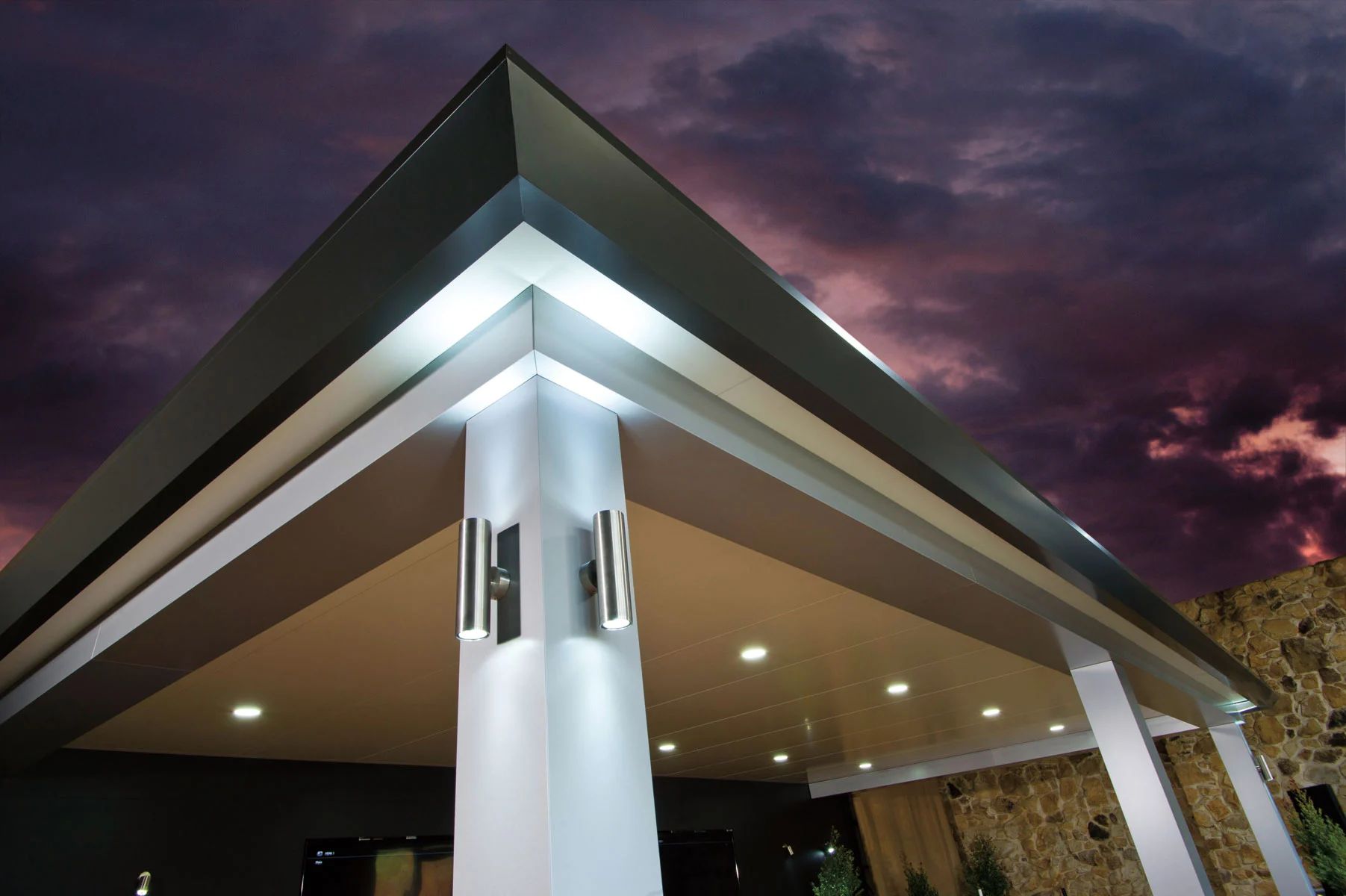 Modern building entrance with white columns and a lit triangular roof at dusk