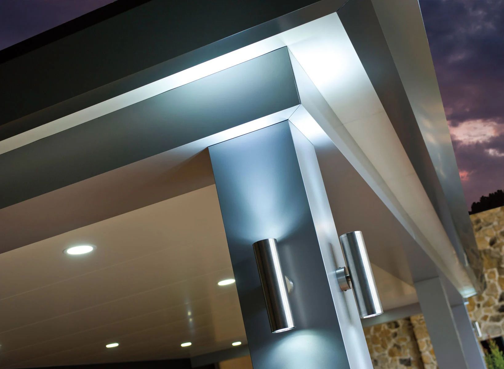 Modern building entrance with lit overhang and metal support column at dusk