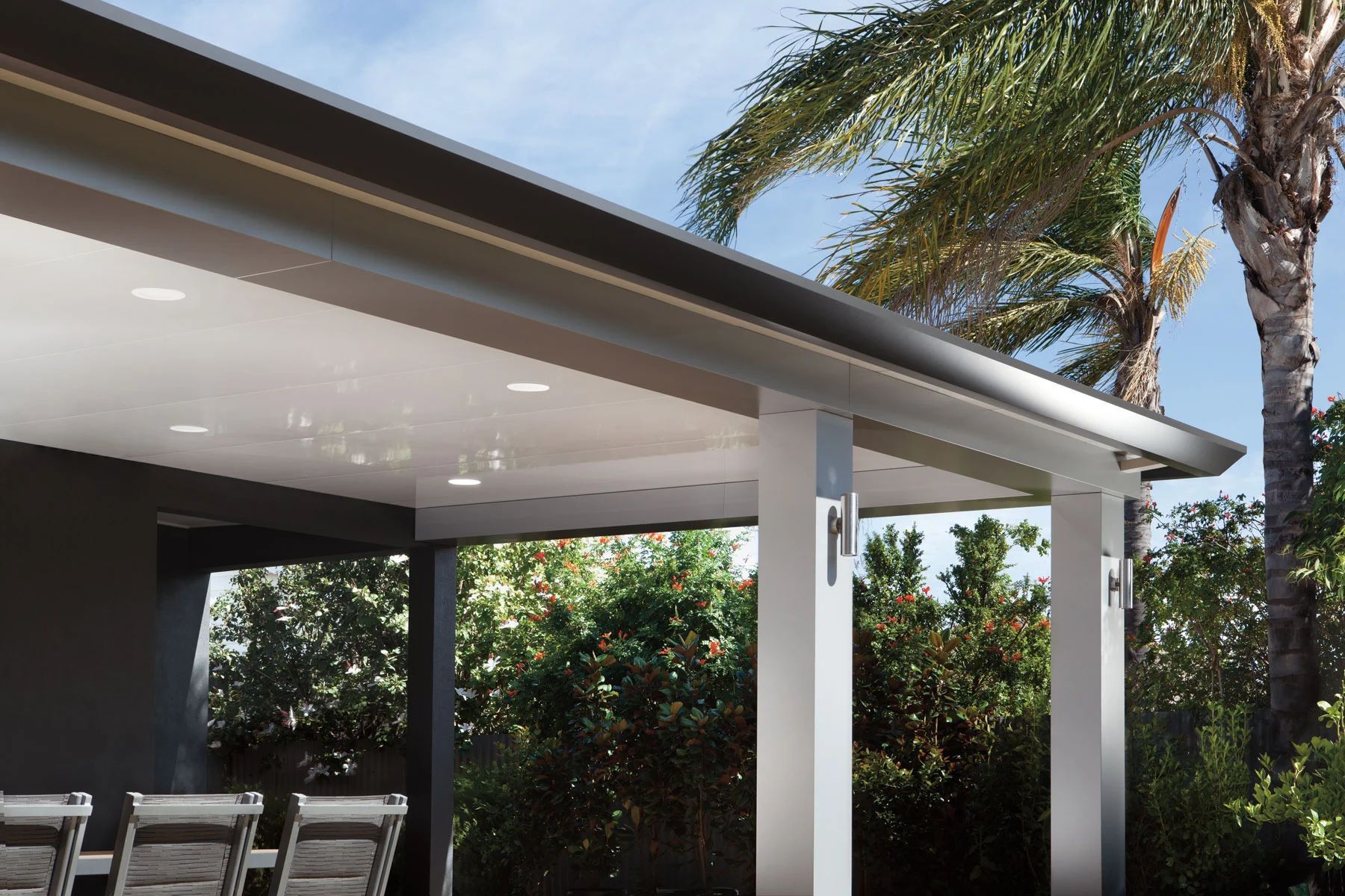 Covered patio with white columns, ceiling lights, and palm trees outside.