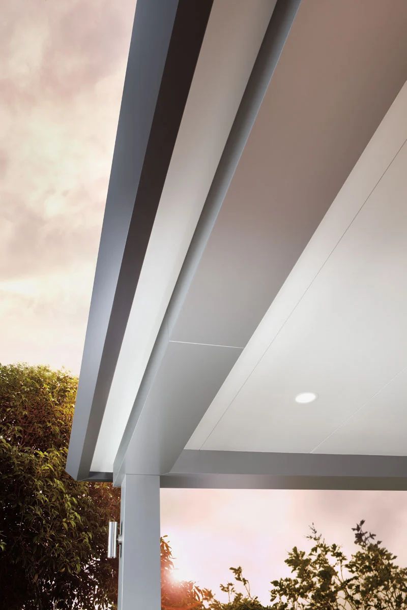 Modern house roof overhang with gray trim and a white ceiling against a cloudy sky and trees