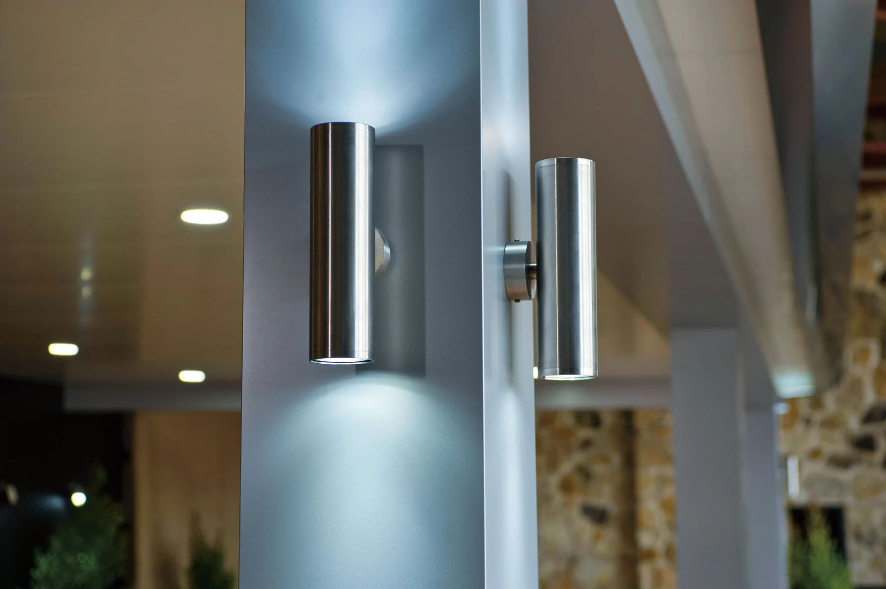 Two modern chrome wall sconces casting soft light on a blue-gray pillar indoors