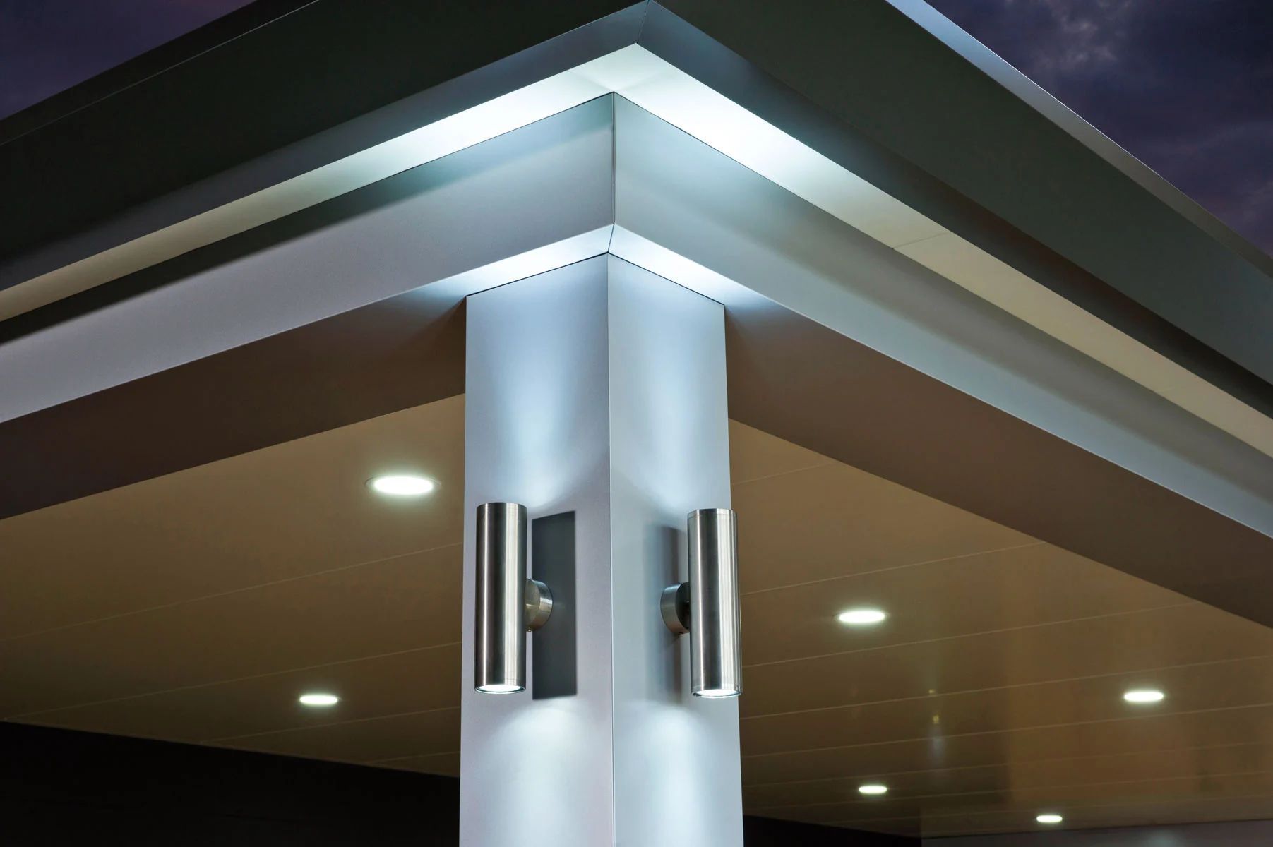 Modern building corner with illuminated roofline and silver support column at night