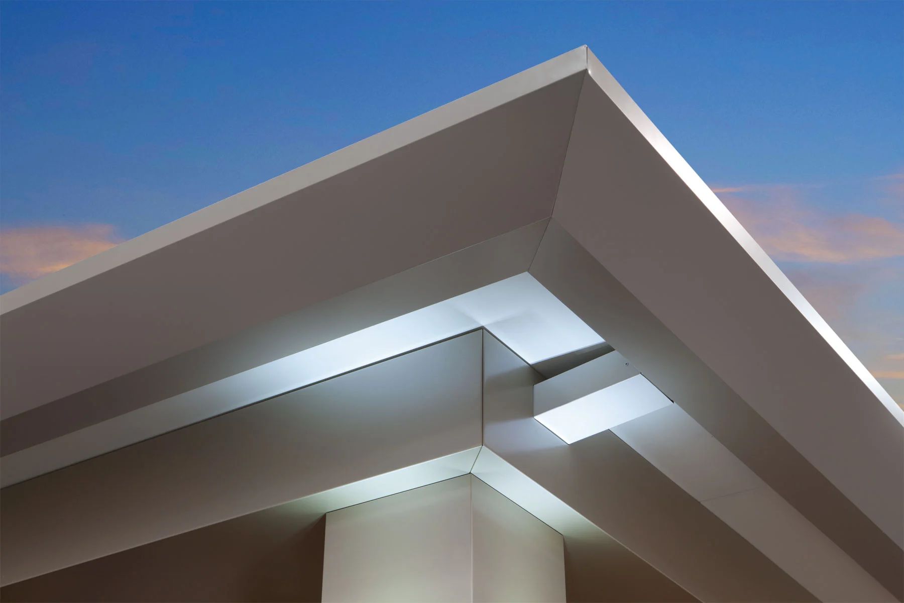 Modern building roof corner with sharp white overhangs against a blue sky