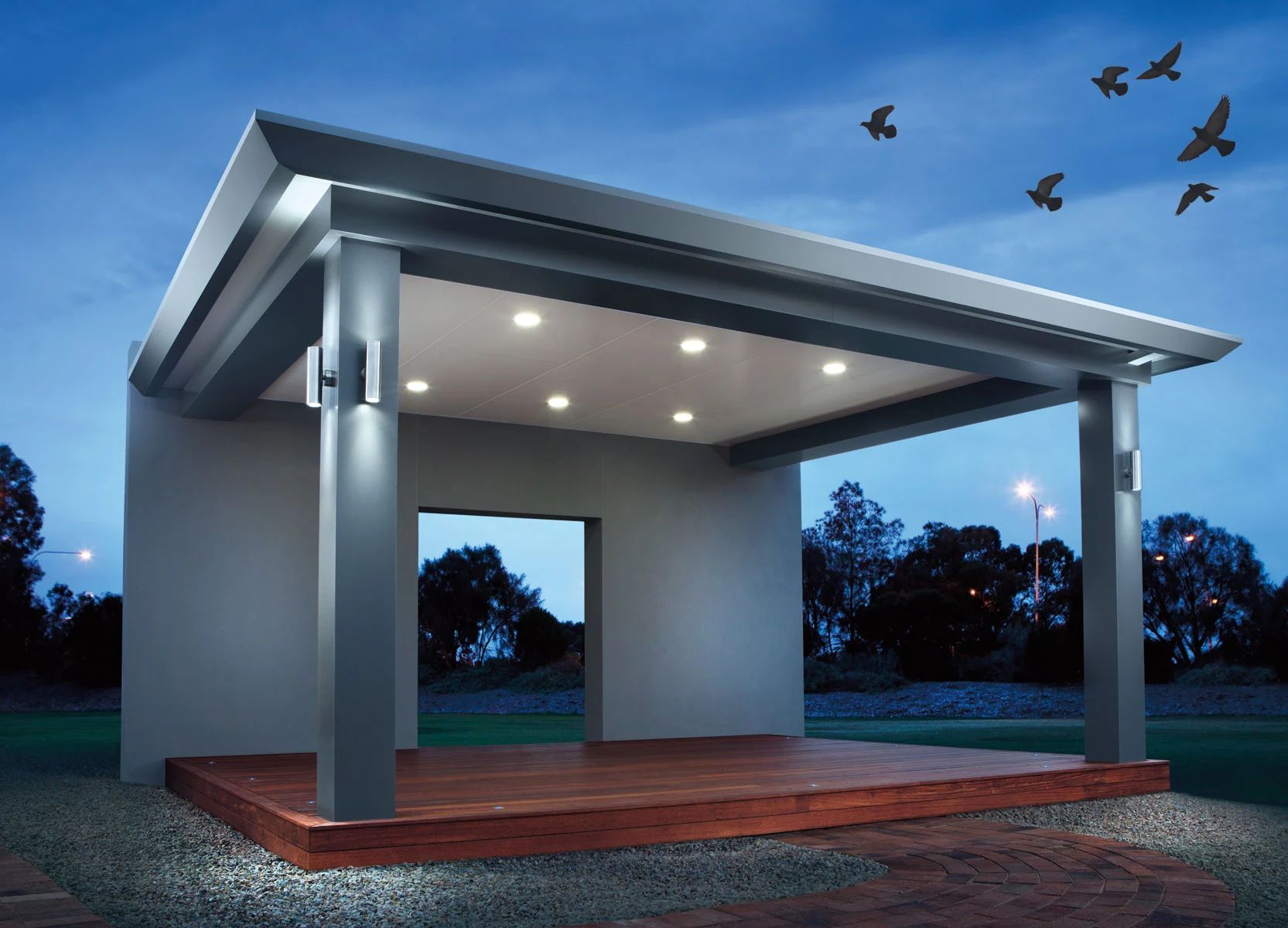 Modern gray outdoor pavilion with lit ceiling lights on a wooden deck at dusk, birds flying overhead