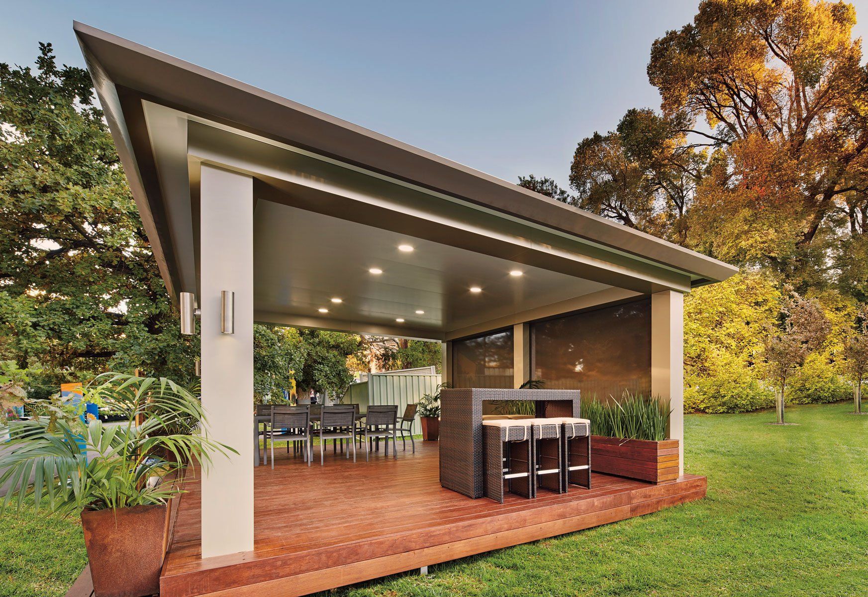 Open-air backyard patio with a modern roof, dining table, and bar stools on a brick floor