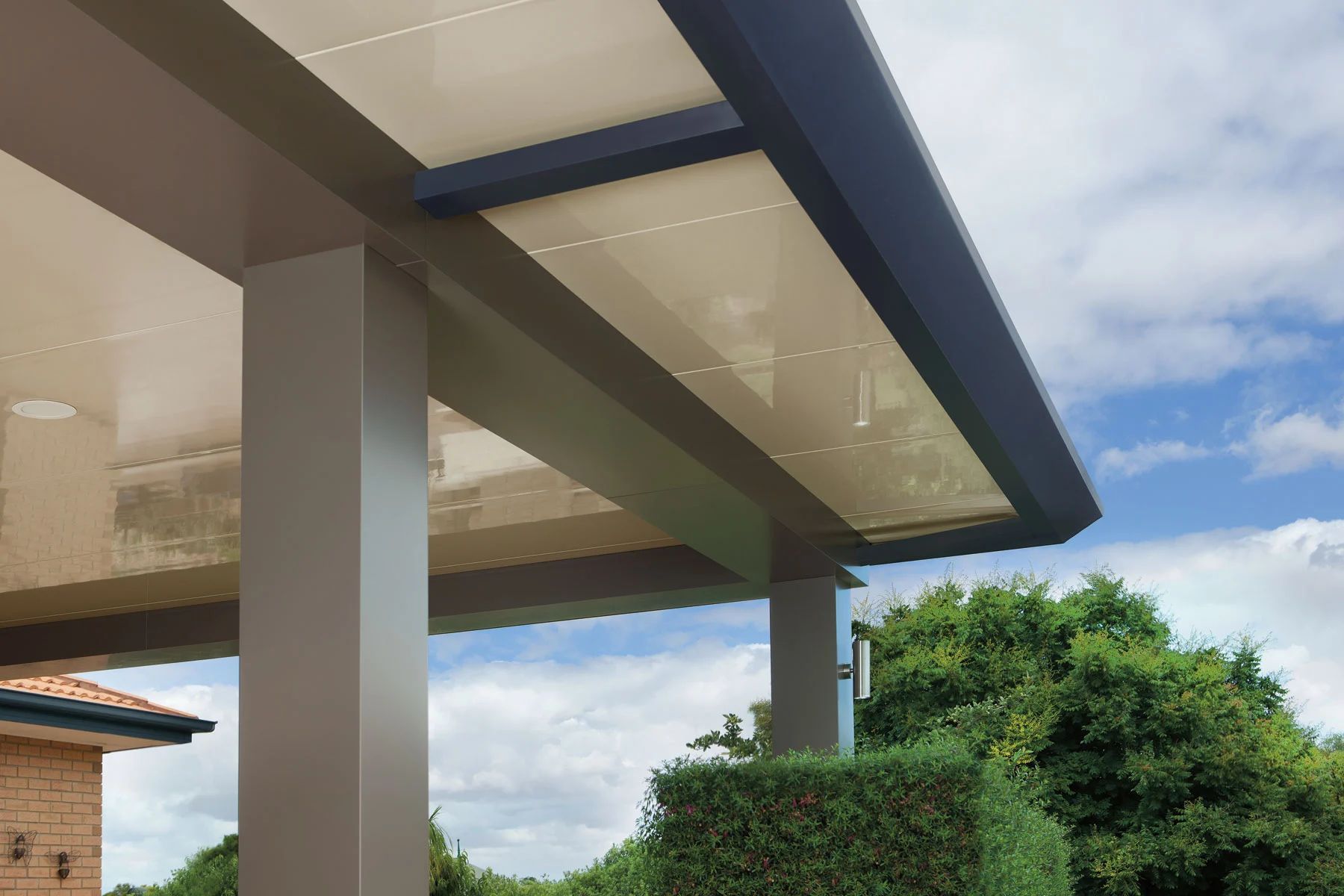 Modern building overhang with white columns, blue trim, and greenery under a cloudy sky