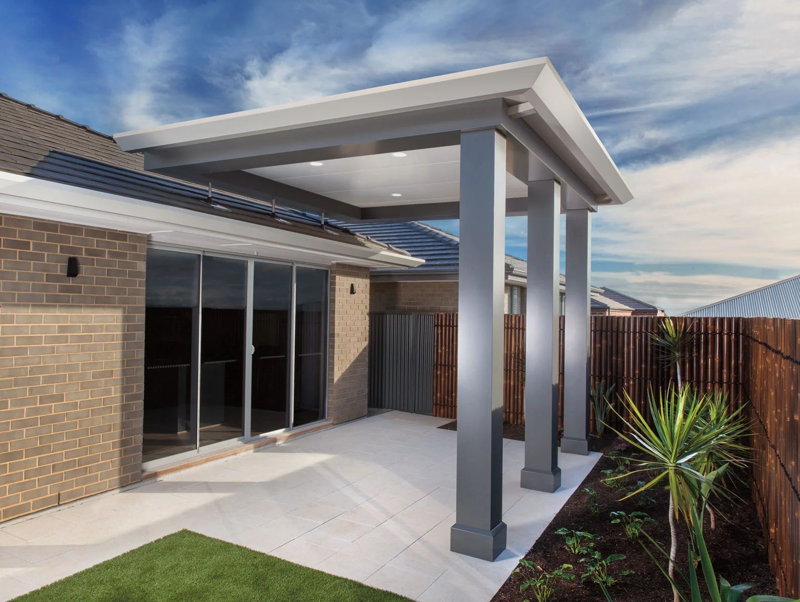 Modern brick patio with sliding glass doors, white paved floor, and a covered pergola beside a wooden fence