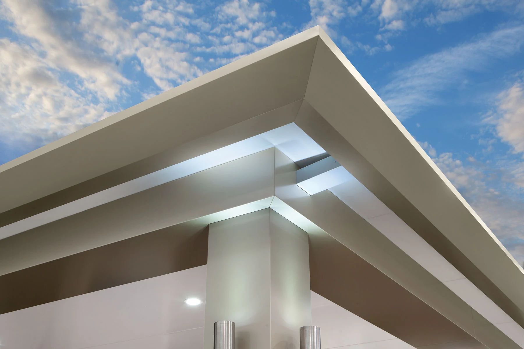 Modern building corner with white overhangs and glass panels against a cloudy blue sky