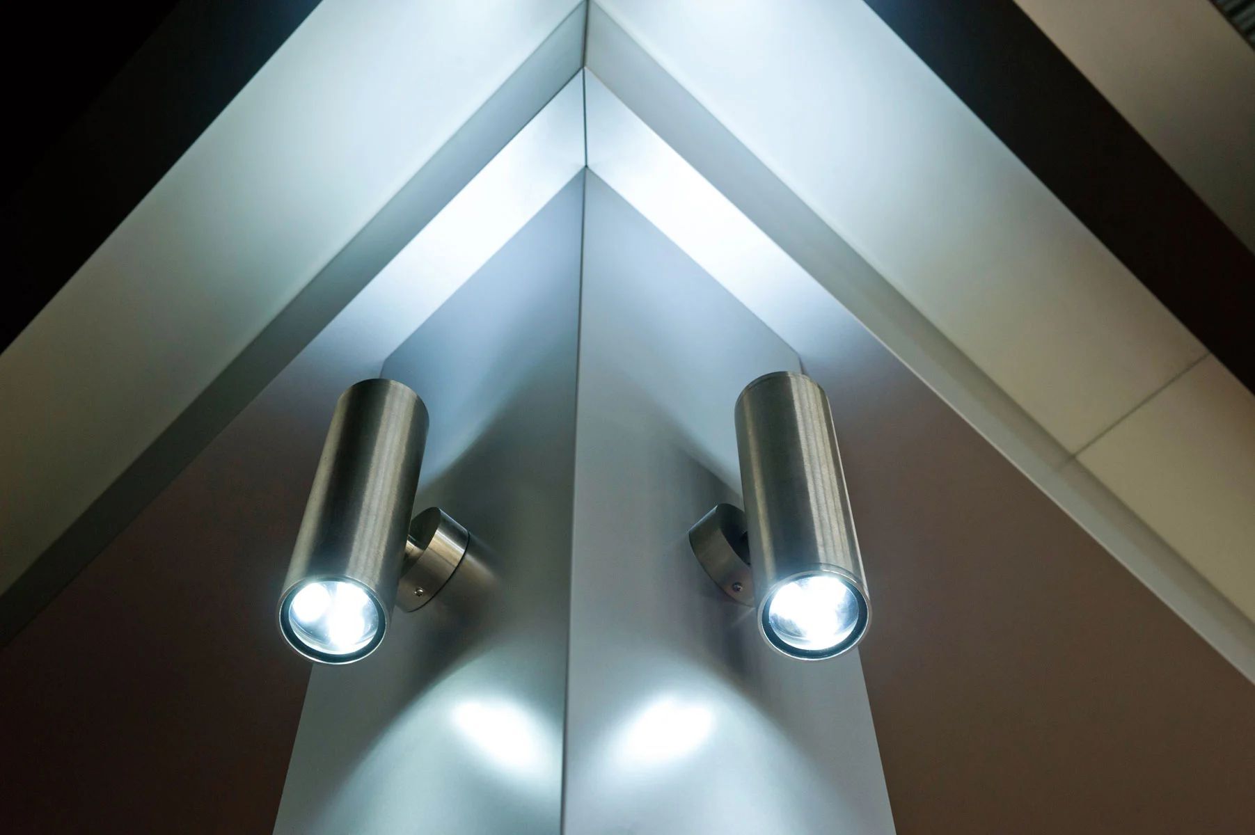 Two silver wall lights illuminating a mirrored triangular ceiling in a modern interior.