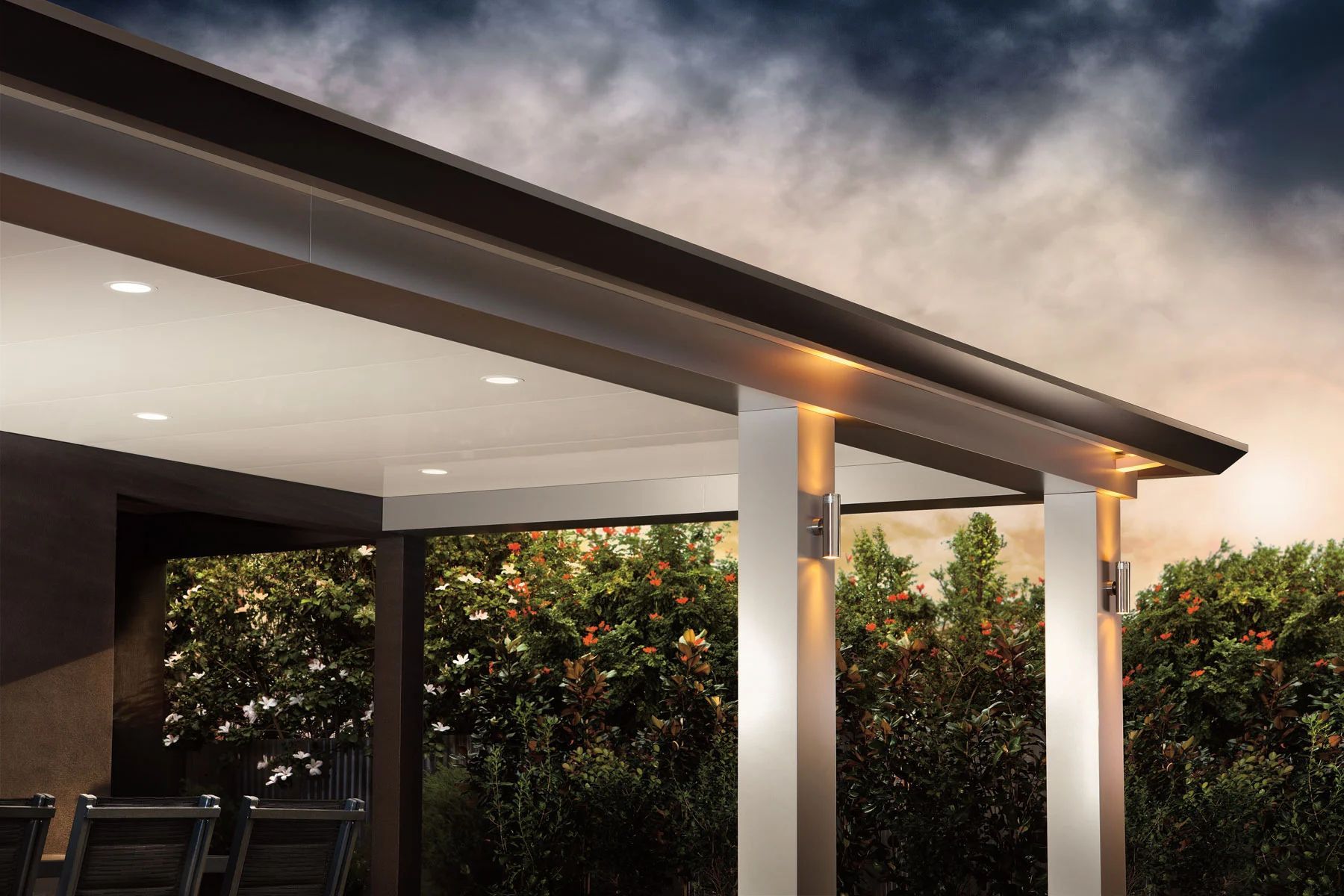 Covered patio roof with white columns, warm lights, and a hedge at dusk
