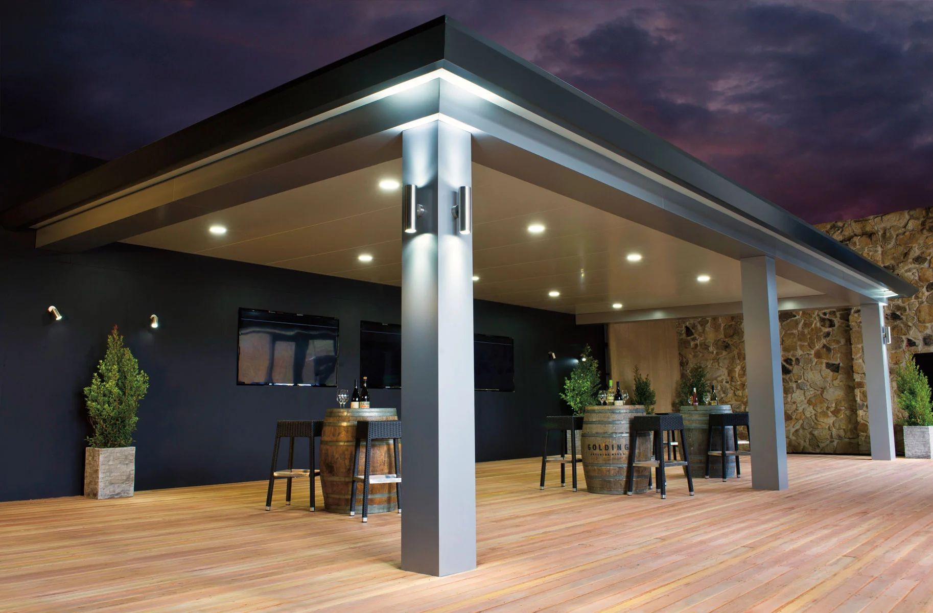 Modern outdoor patio with bar seating, wooden deck, and dark roof under evening sky.