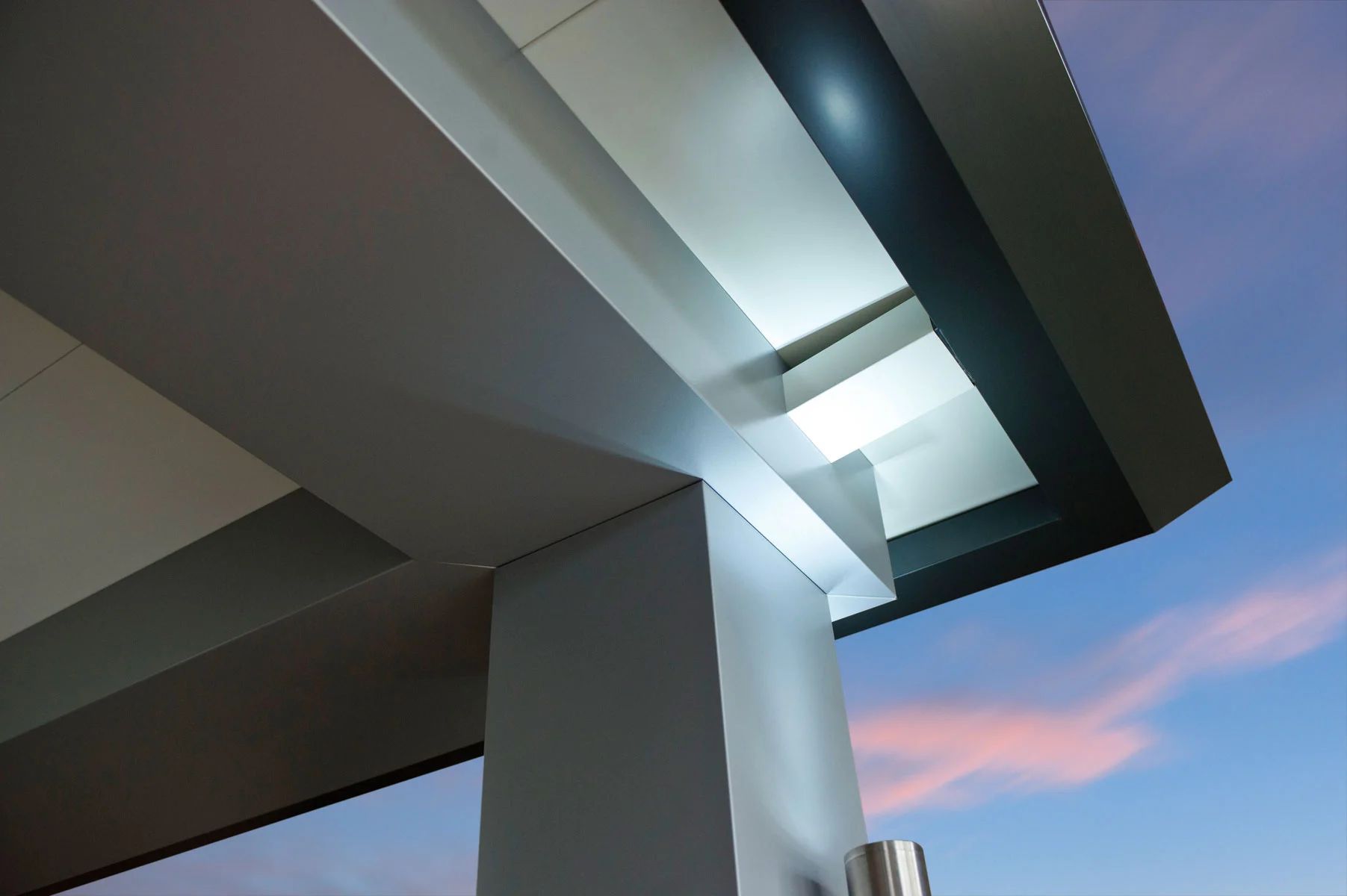 Modern building overhang with glass skylight against a pink evening sky