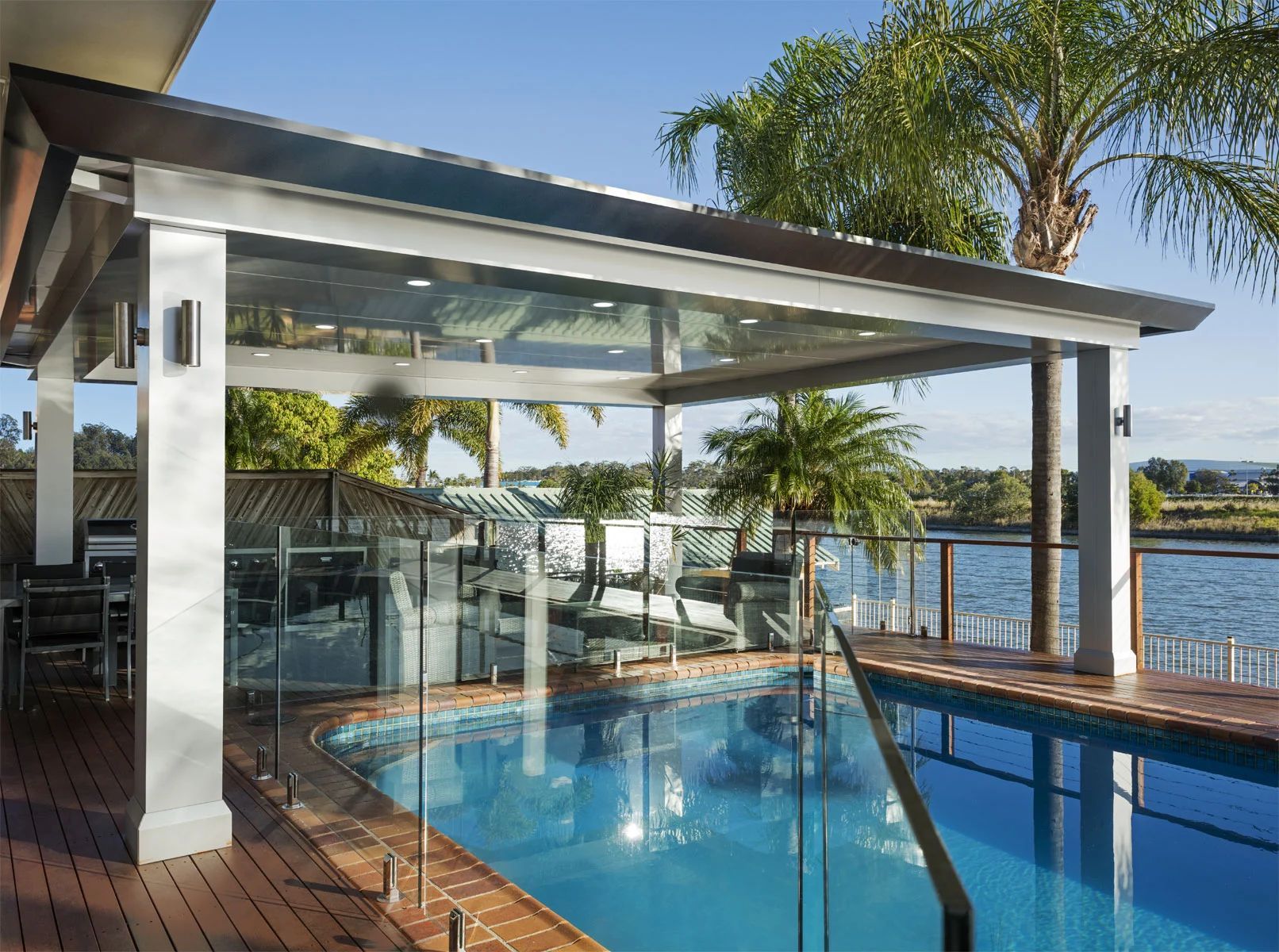 Modern patio with a glass-walled pool, lounge chairs, and ocean view under a sunny sky