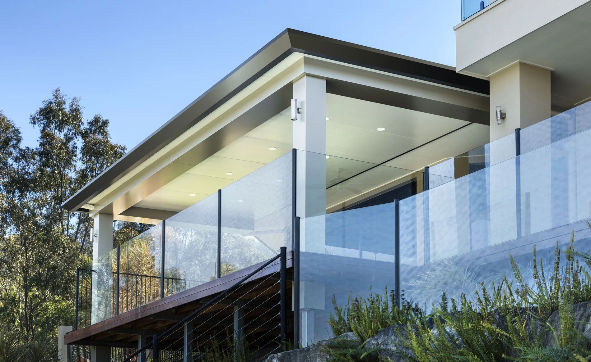 Modern house balcony with glass railing and white columns under a clear sky