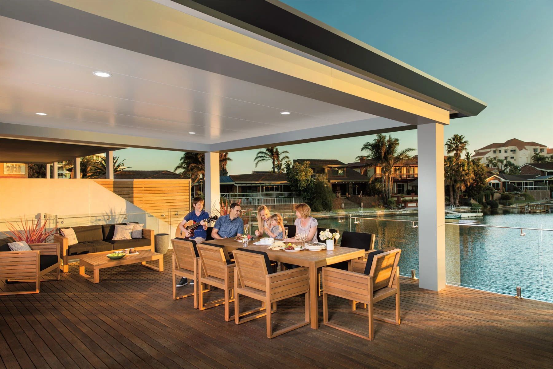 People dining on a waterfront patio at sunset beside a pool and marina