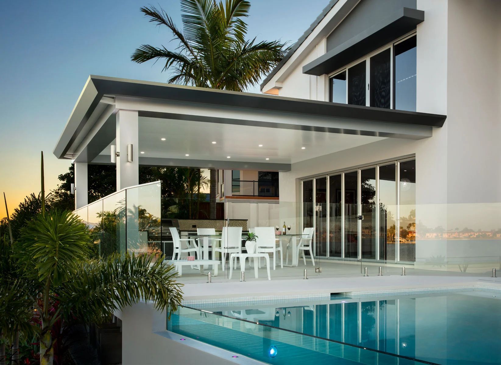 Modern white patio with pool, glass doors, and outdoor dining area at a contemporary house.