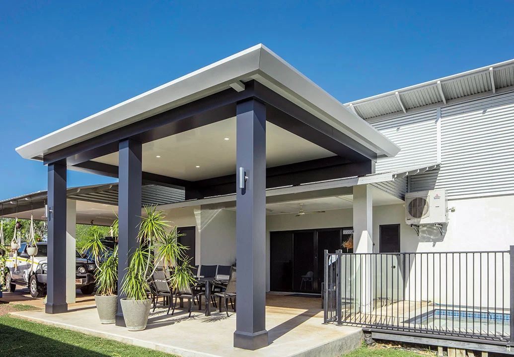 Modern house exterior with a covered patio, dark columns, and a fenced yard