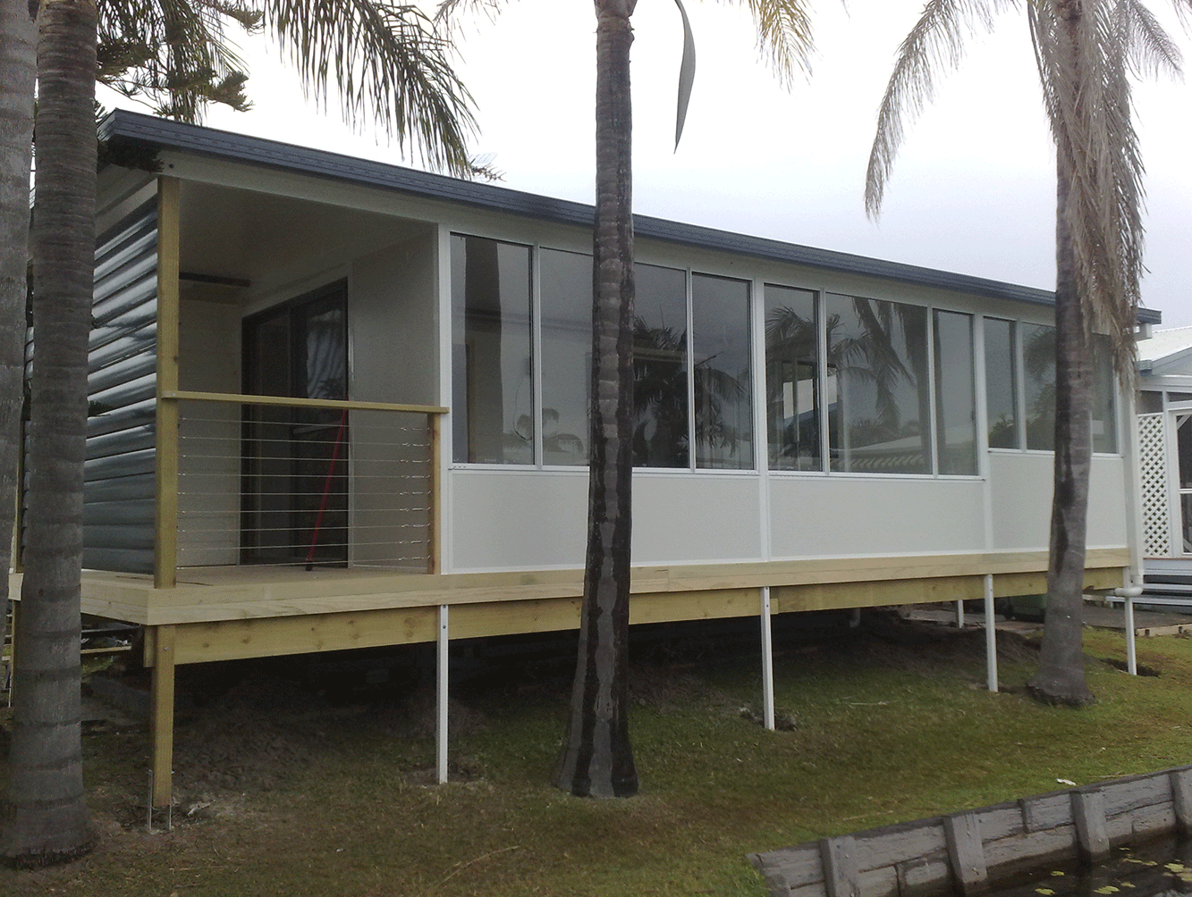 Small white raised house with a porch, screened windows, and palm trees in front