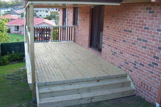 Wooden porch deck with steps beside a brick house, overlooking a backyard and neighboring homes.